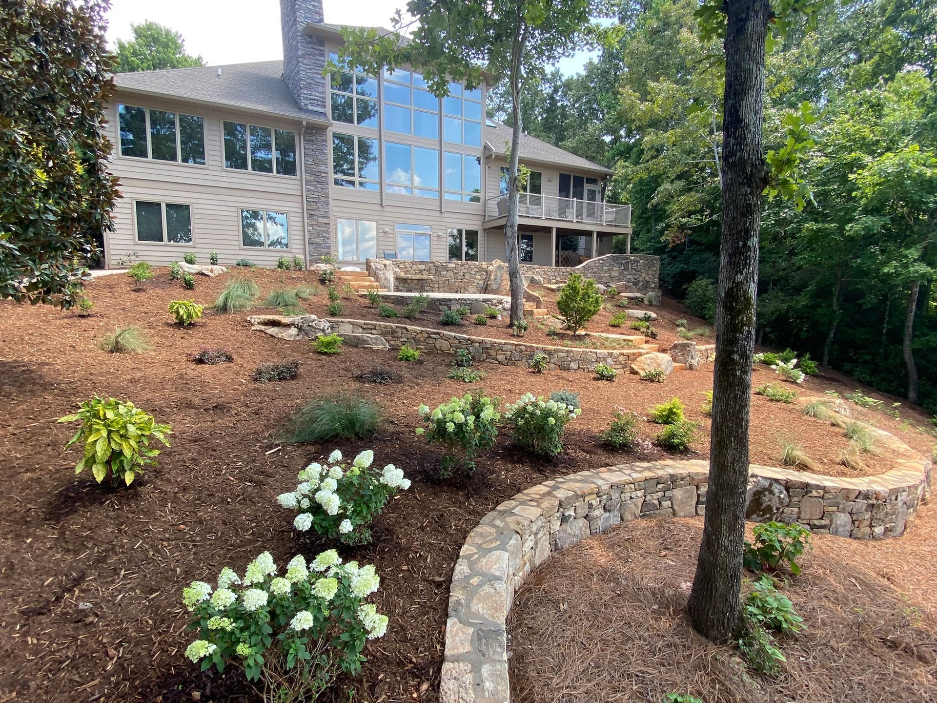 A large house with a lot of windows is surrounded by trees and flowers.