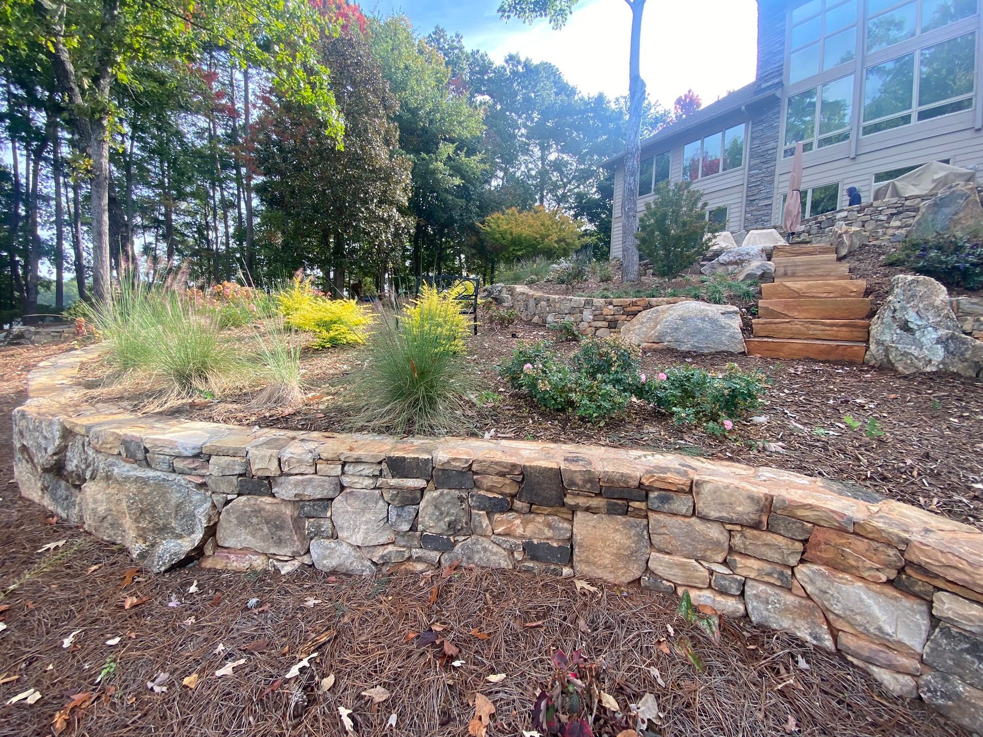 A stone wall with stairs leading up to a house in the background.