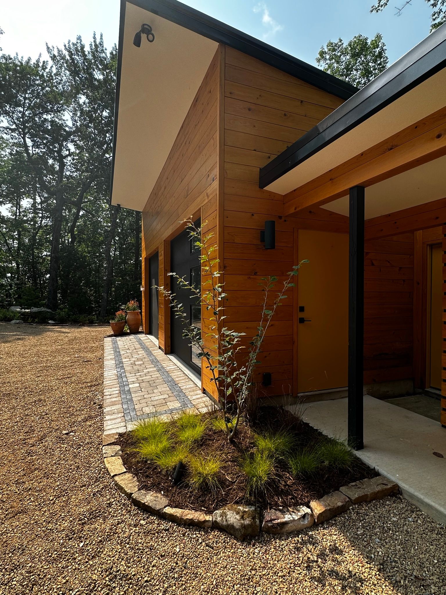 A wooden house with gravel in front of it and trees in the background.