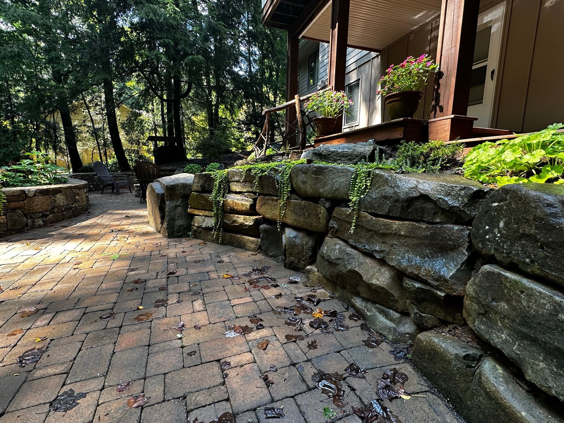 A stone wall surrounds a brick walkway leading to a house.