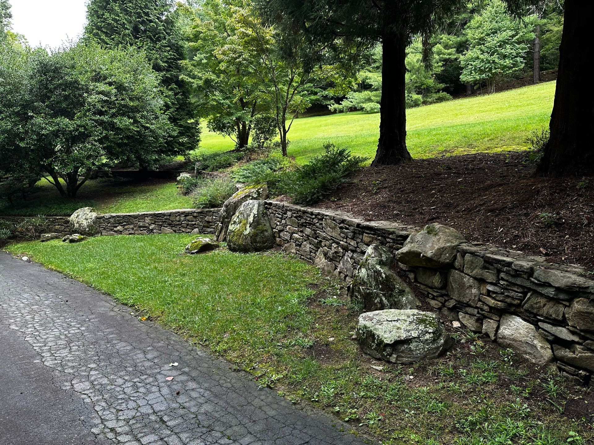 A stone wall is surrounded by grass and trees in a park.