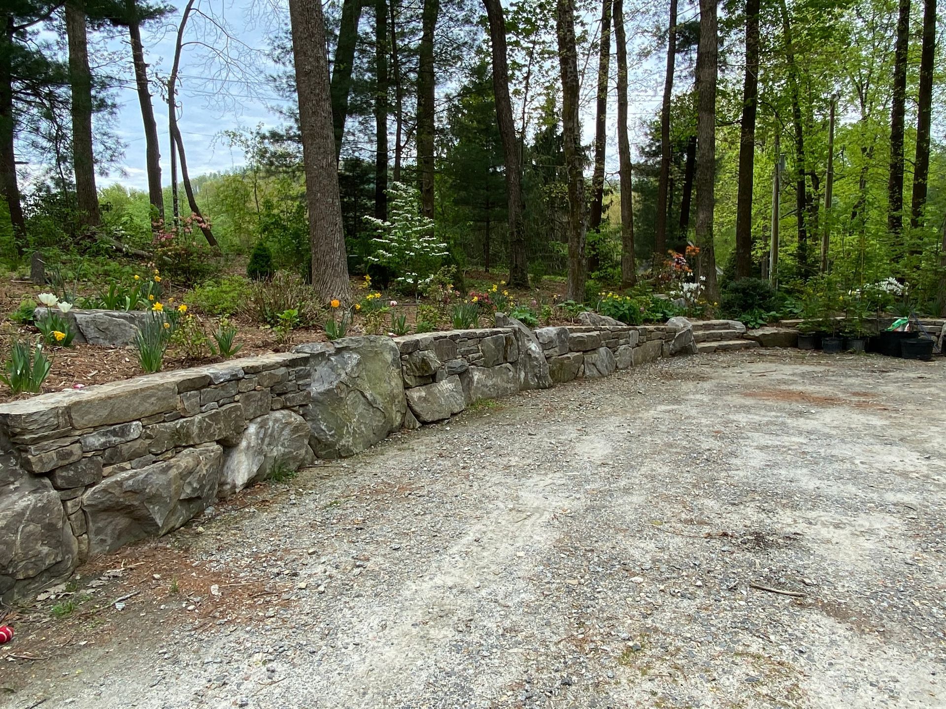 A gravel driveway with a stone wall and trees in the background.
