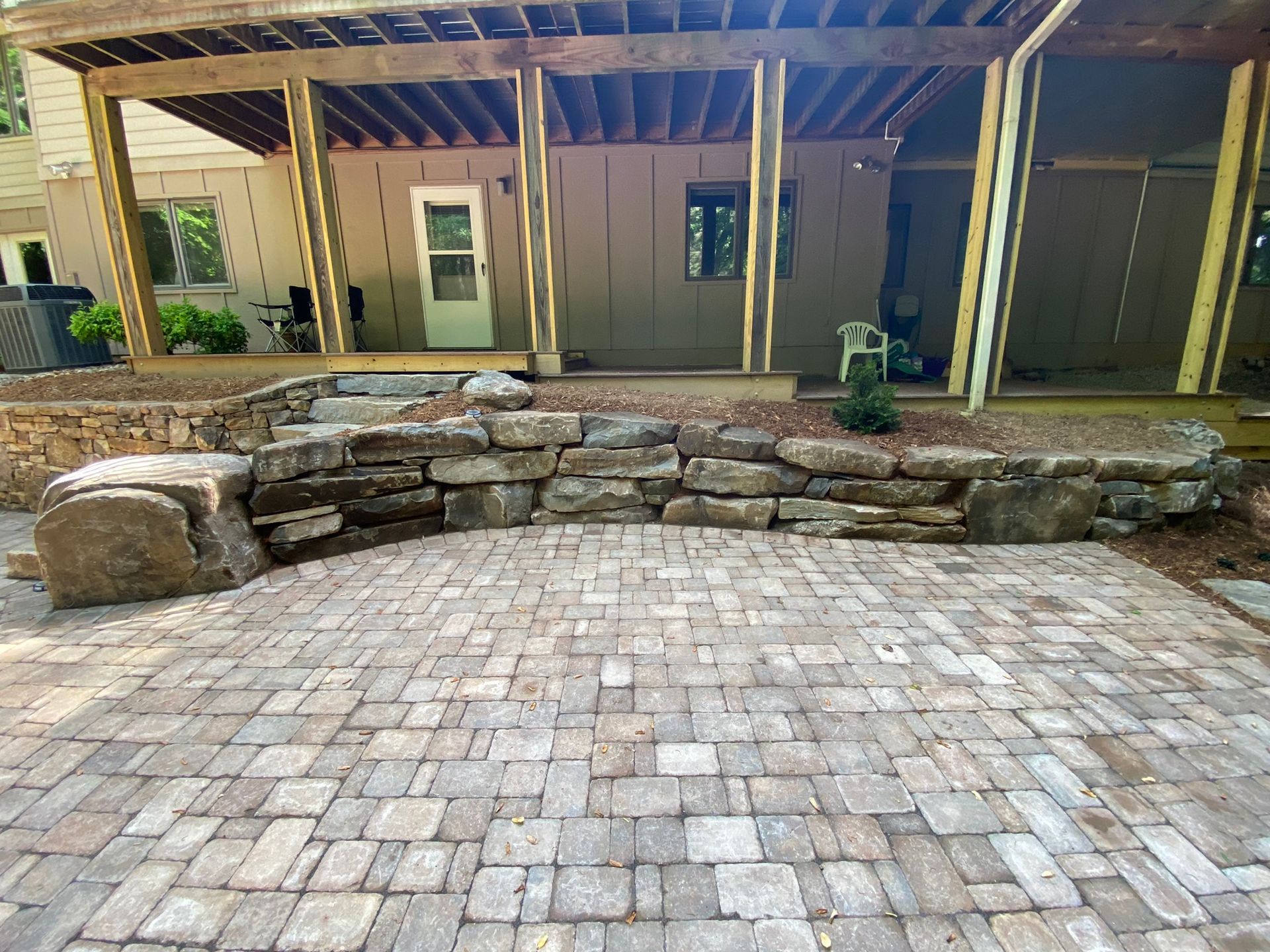 A brick patio with a stone wall in front of a house.