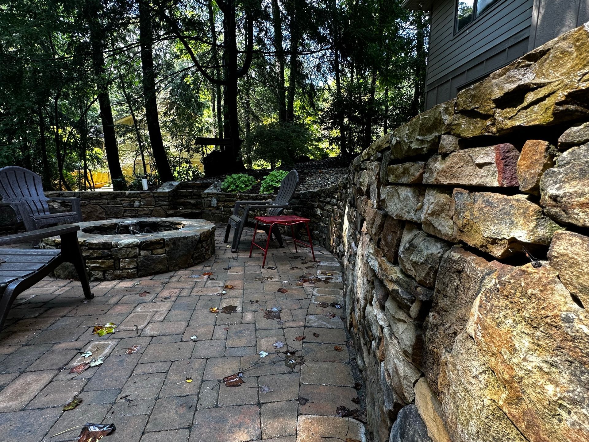 A stone wall surrounds a patio with a fire pit and chairs.