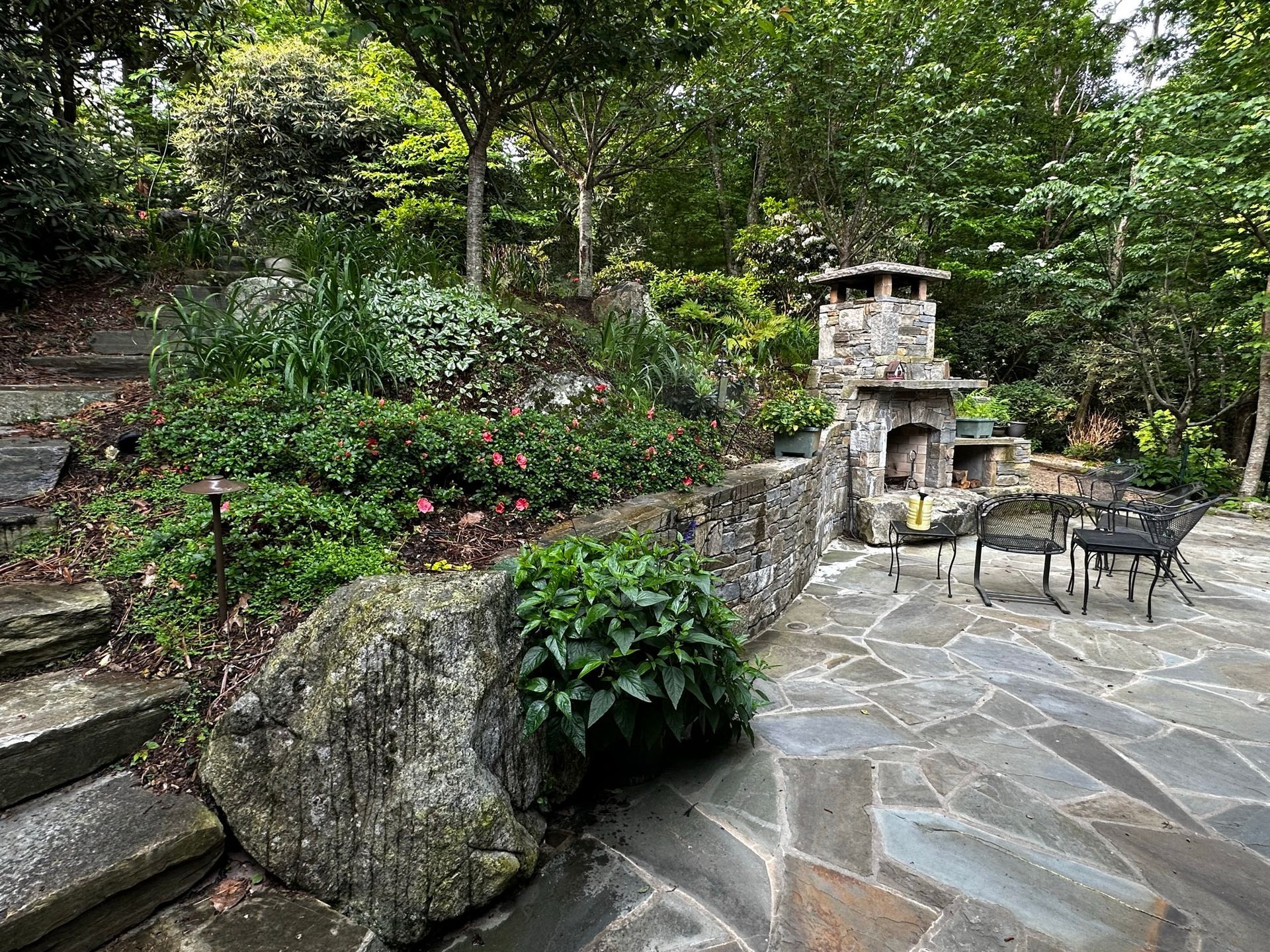 A stone patio with a fireplace and stairs in a backyard.