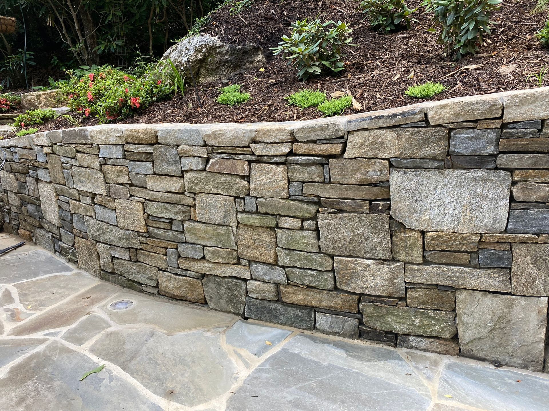 A stone wall with a patio in front of it in a garden.