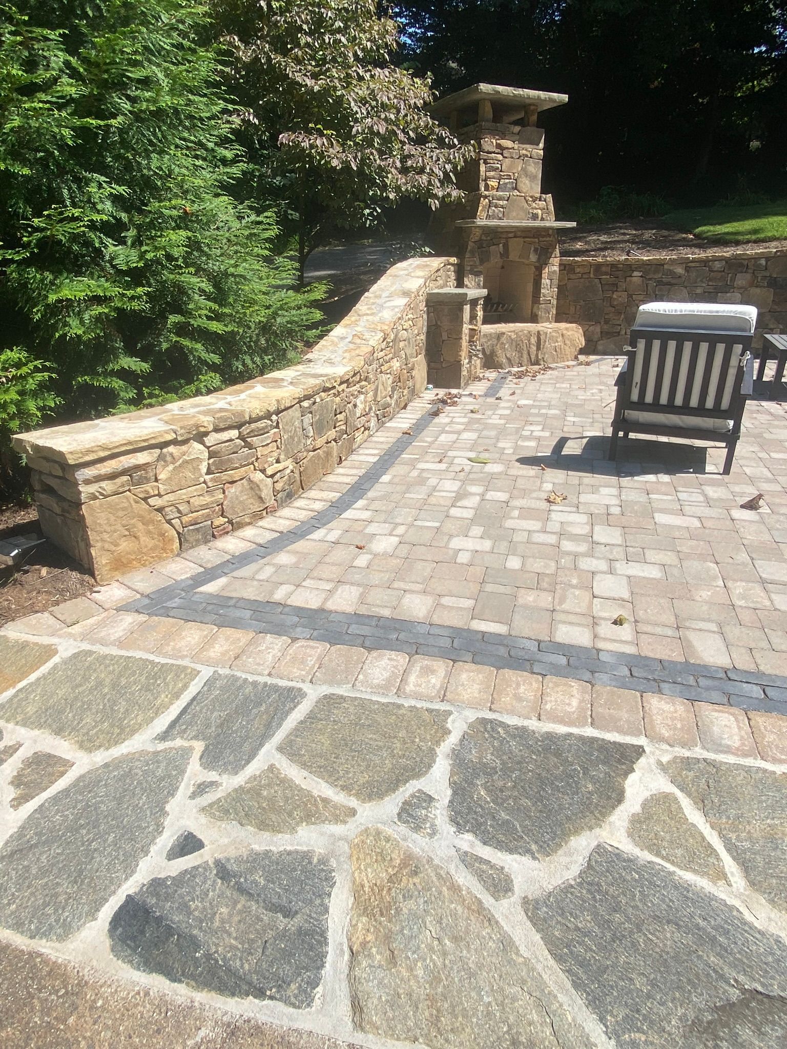 A stone patio with a chair and a stone wall.