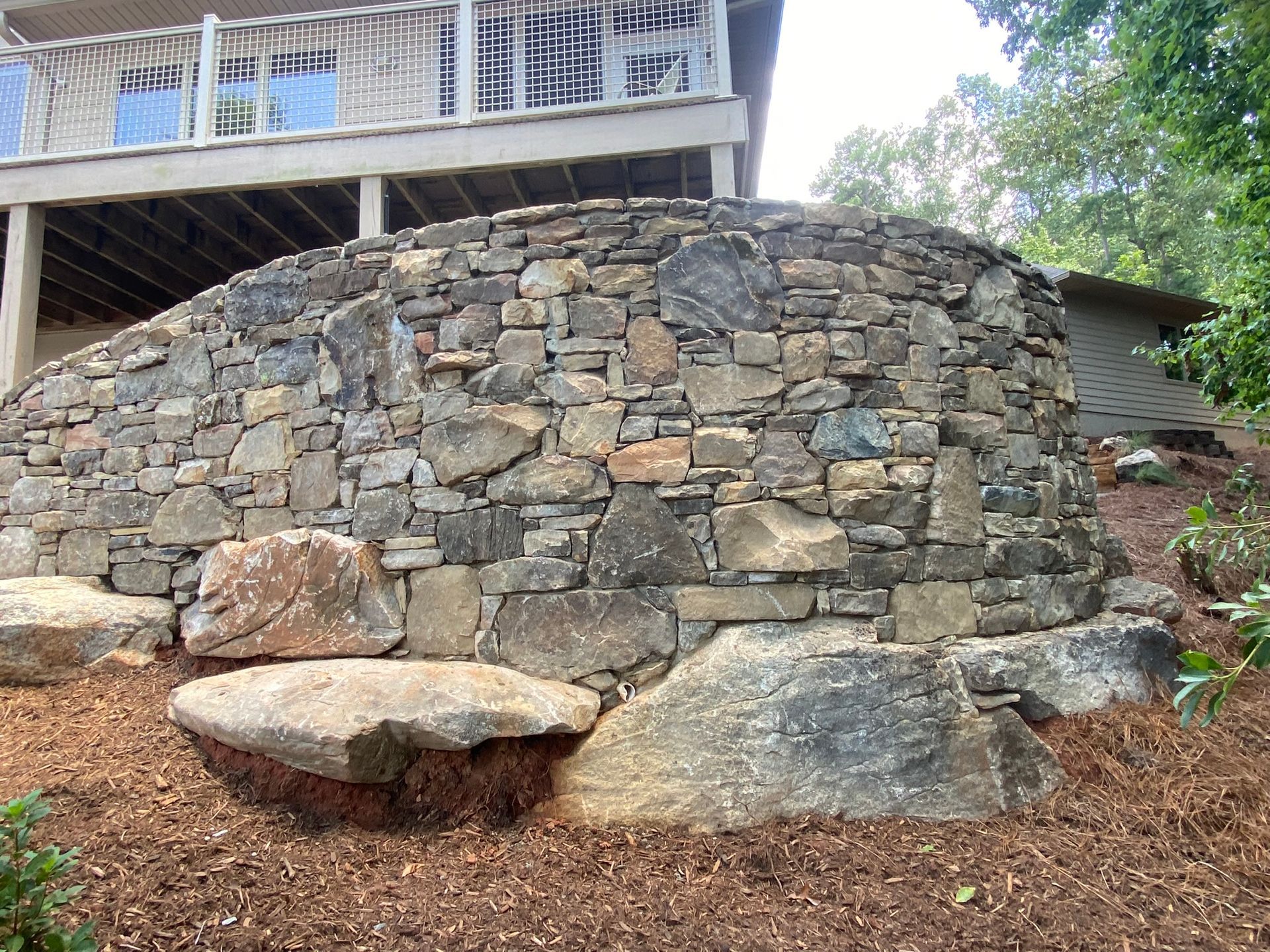 A large stone wall is in front of a house with a deck.