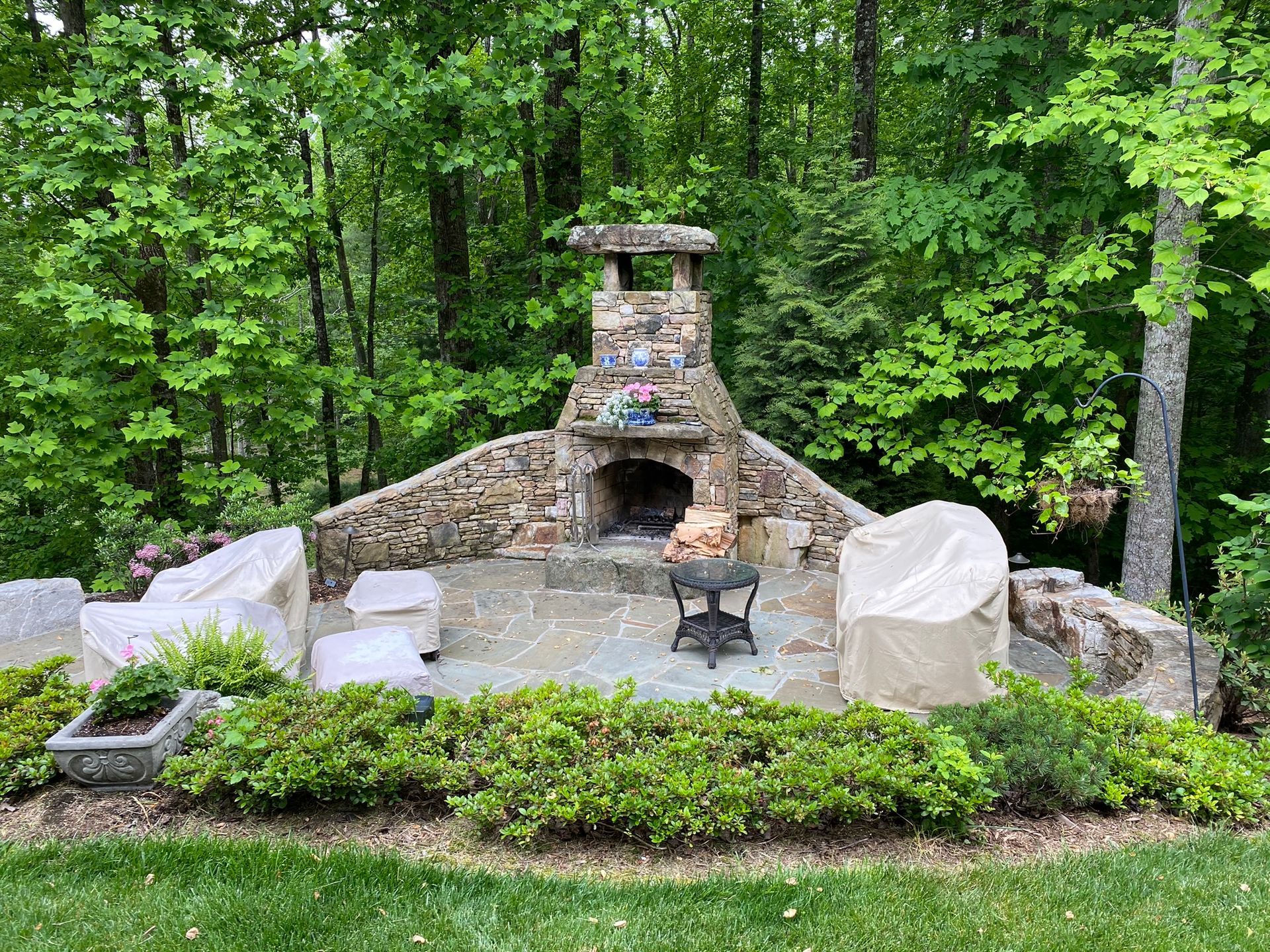 There is a fireplace in the middle of the backyard surrounded by trees.