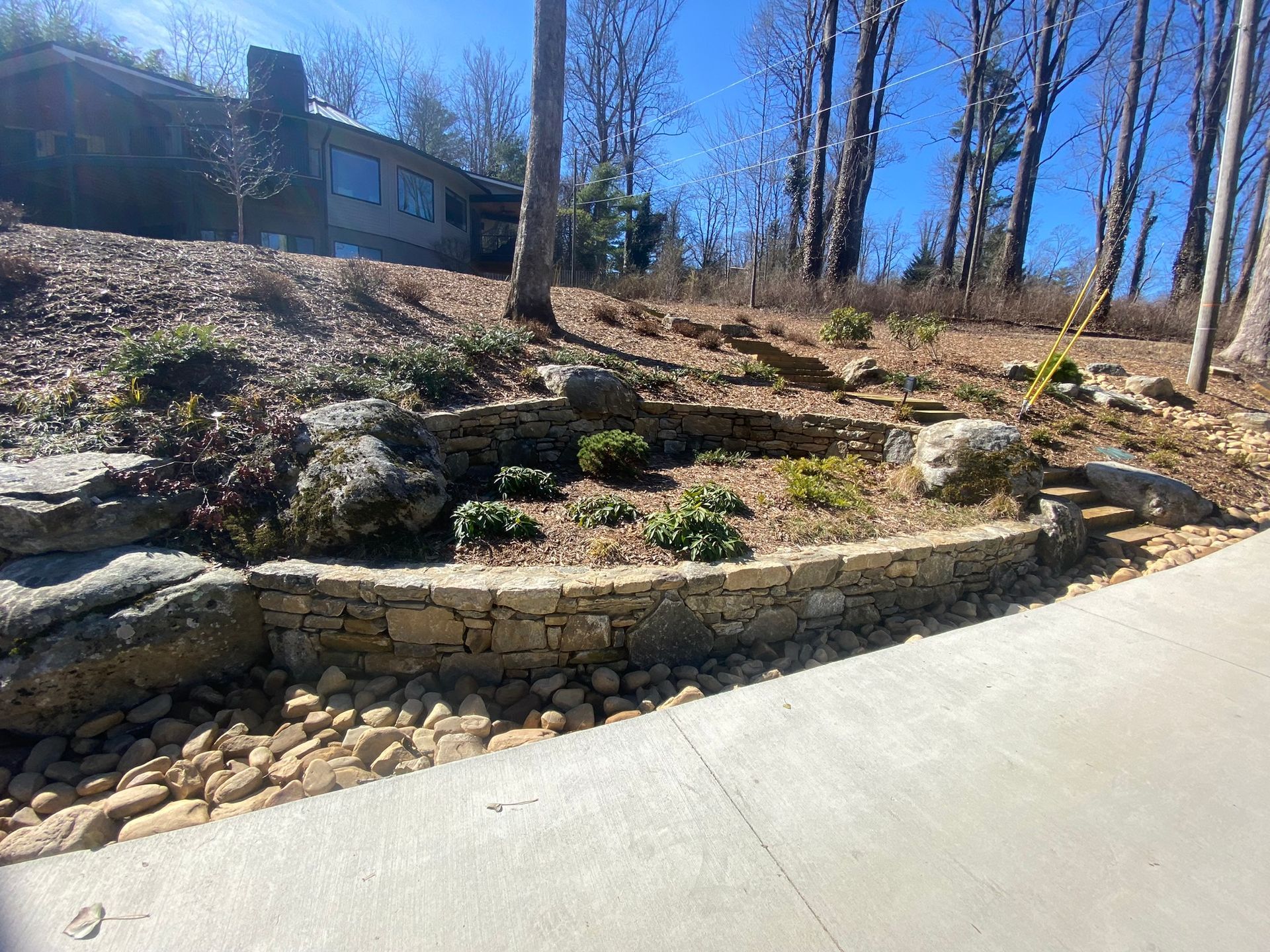 A stone wall surrounds a lush green garden in front of a house.