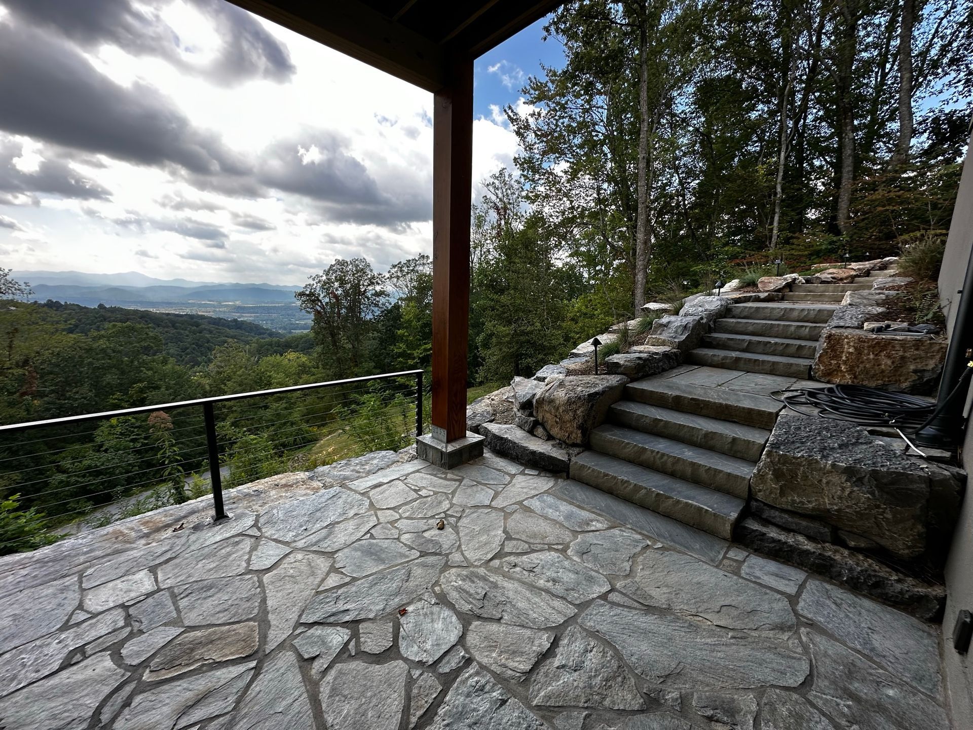 A stone patio with stairs leading up to a view of a forest.