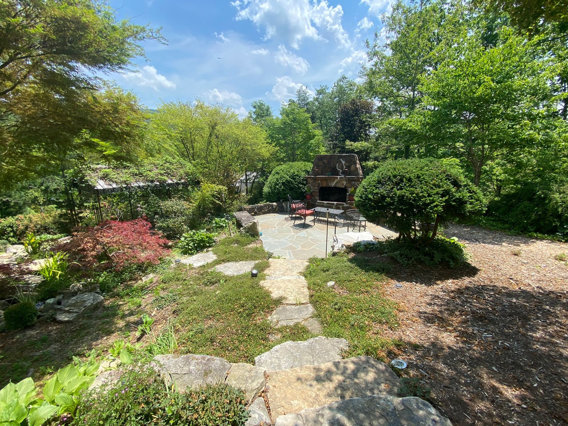 A backyard with a patio and a fireplace surrounded by trees and bushes.