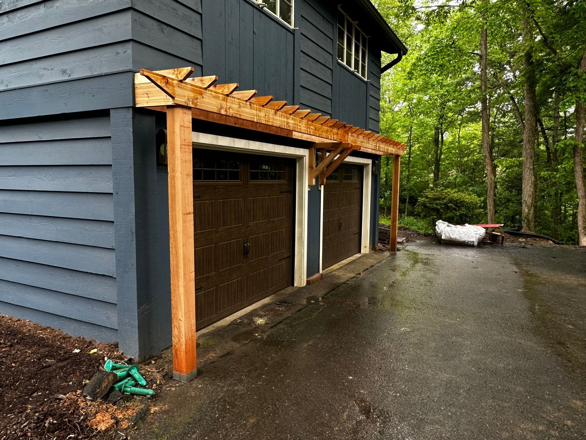 A blue house with a wooden pergola over the garage doors.