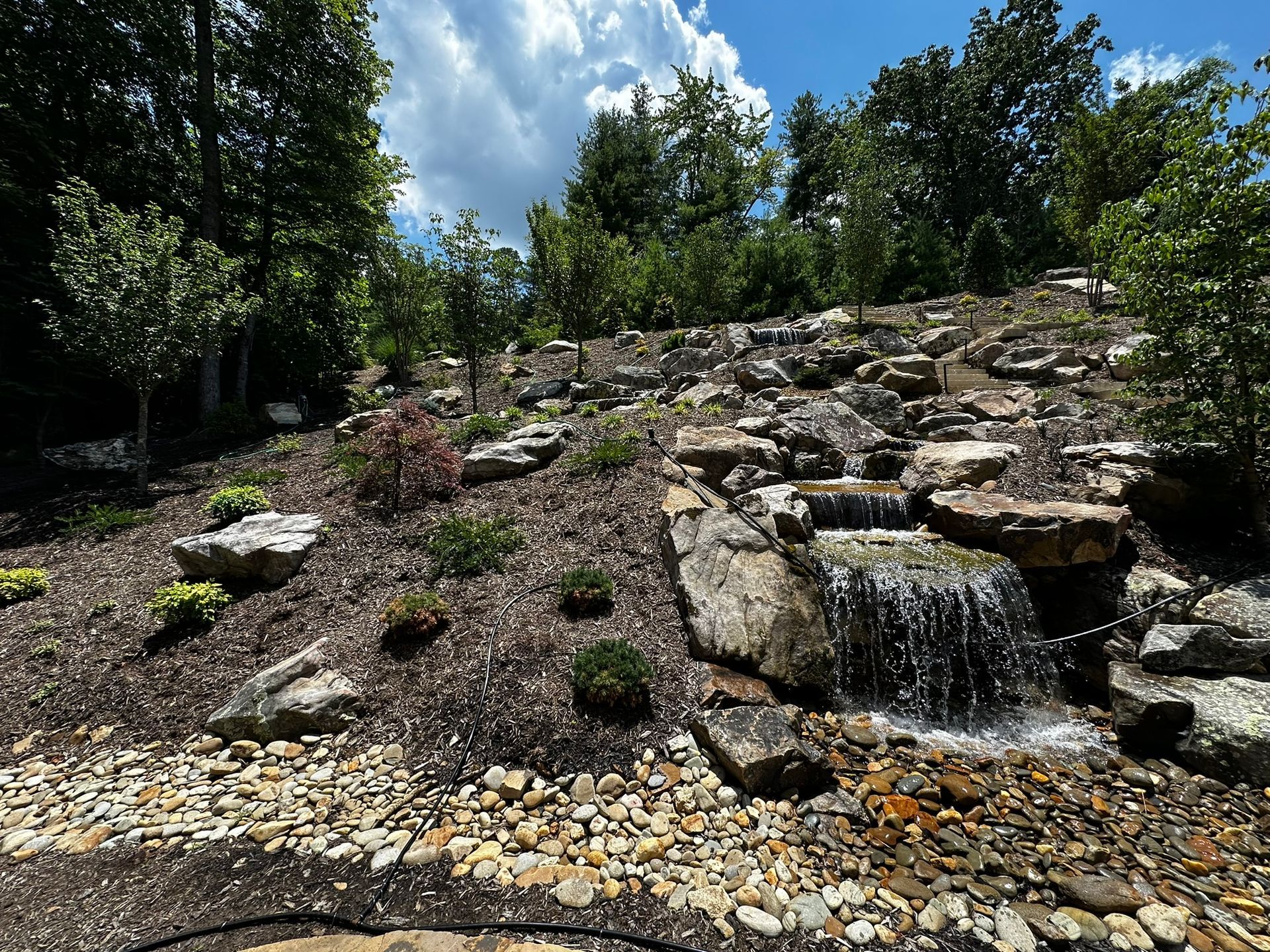 A waterfall is surrounded by rocks and trees in a garden.