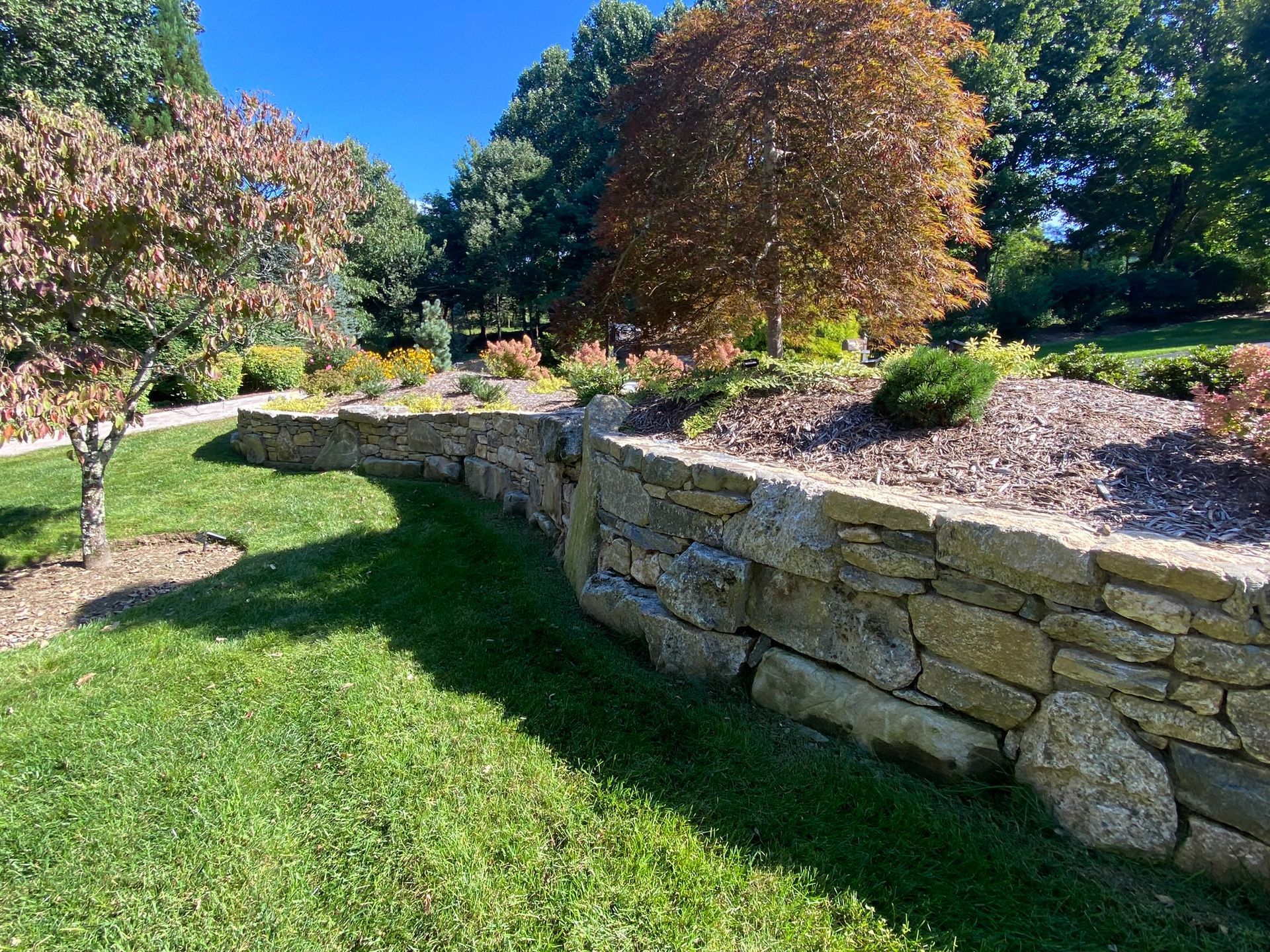 A stone wall surrounds a lush green lawn in a park.