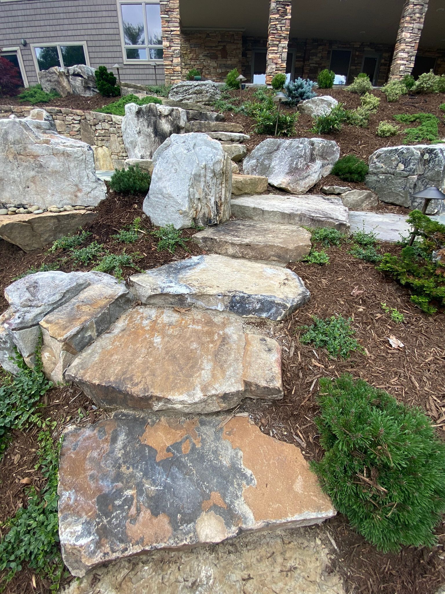 A stone walkway leading up to a house surrounded by rocks and plants.