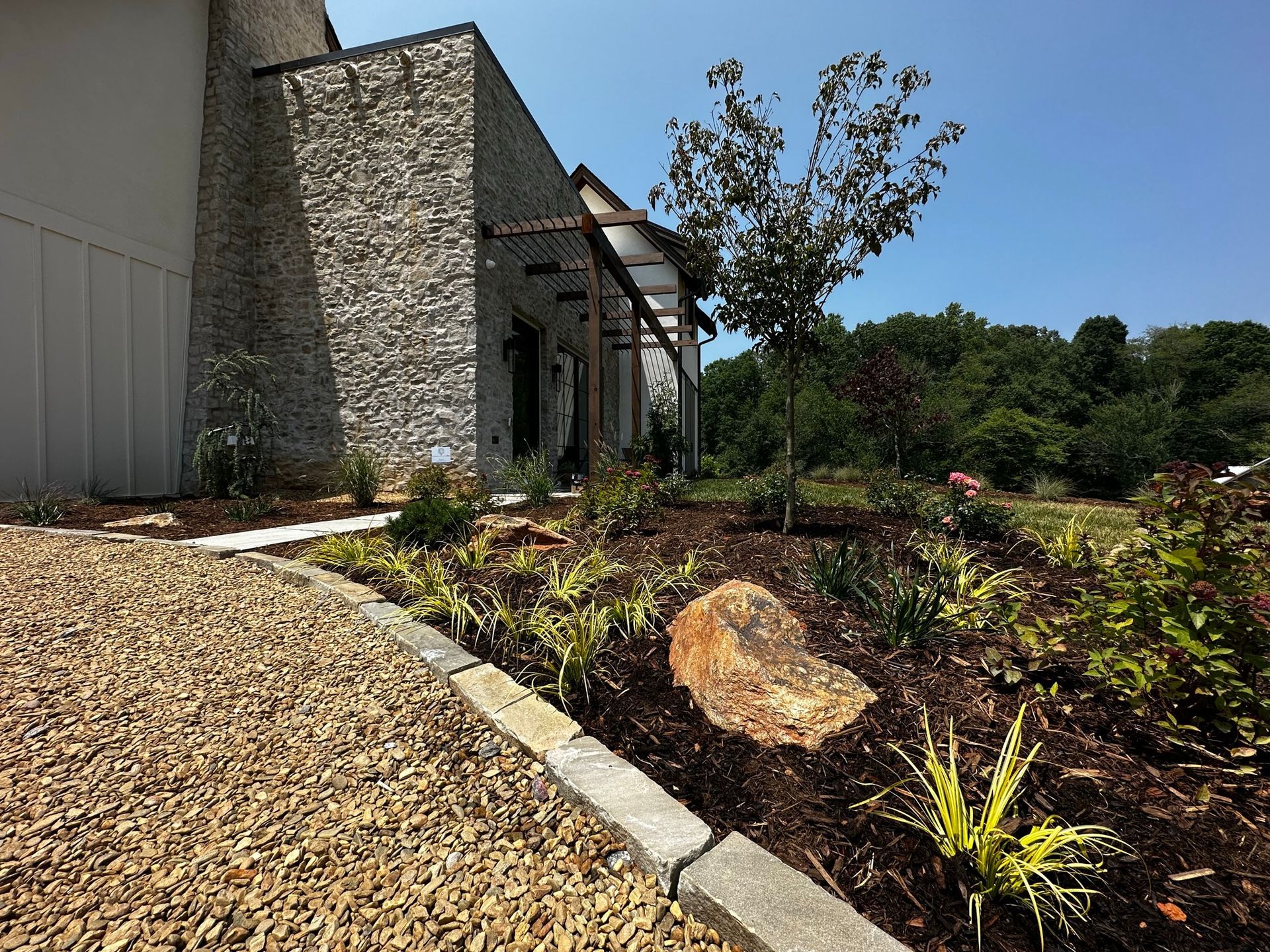 A gravel driveway leading to a house with a stone wall.