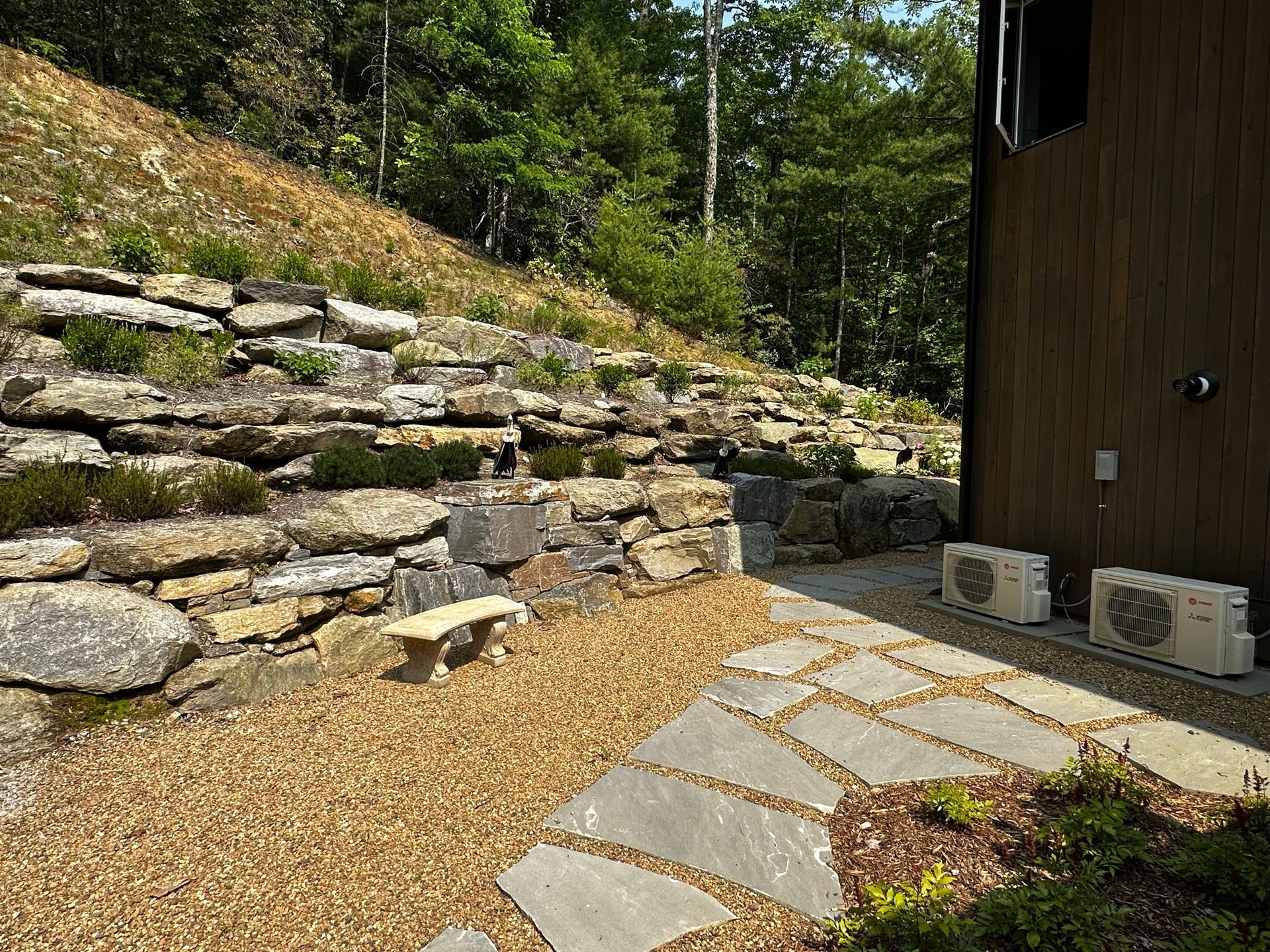 A stone walkway leading to a house with a stone wall in the background.
