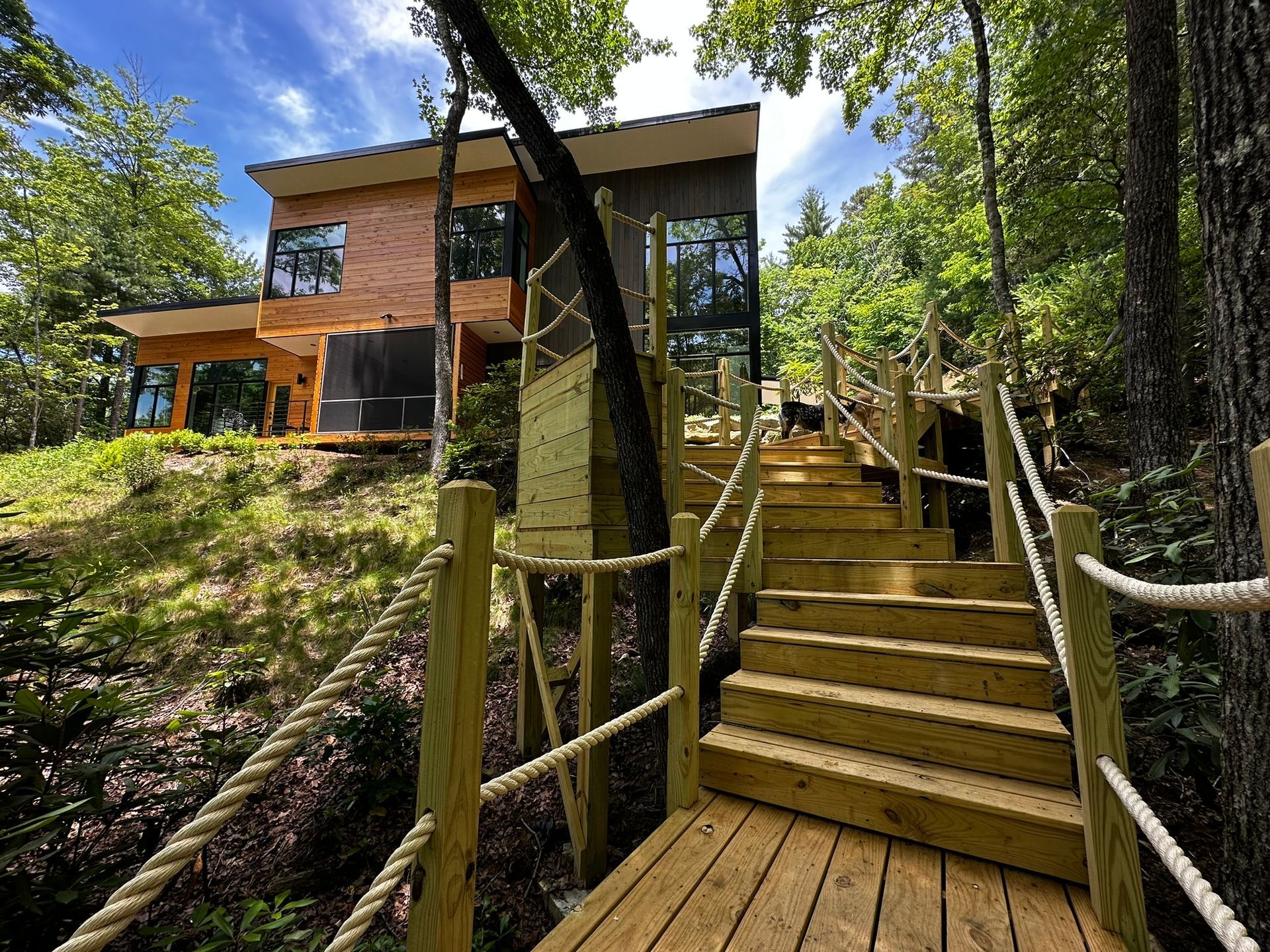 A wooden bridge leads to a house in the woods.