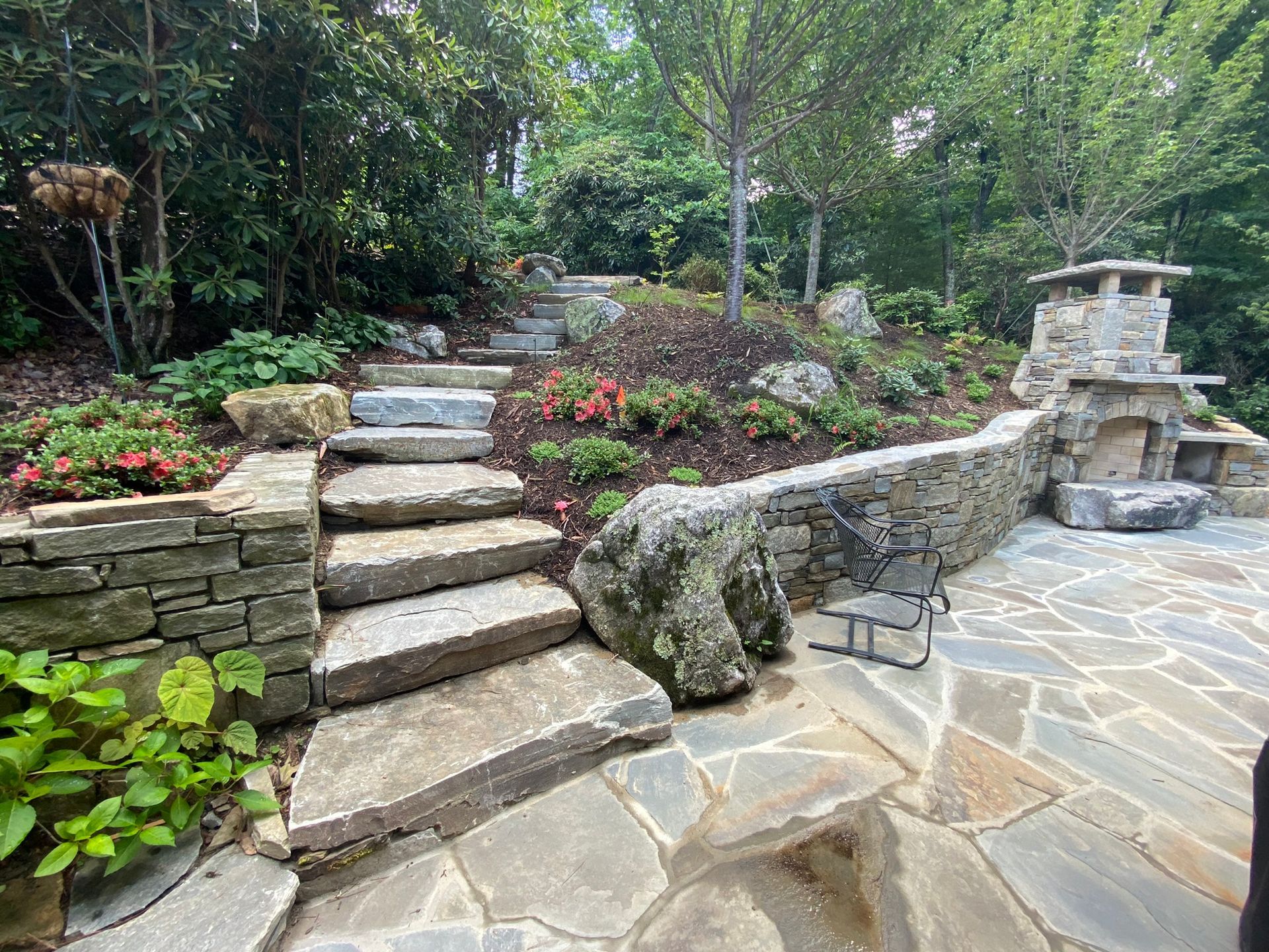 A stone patio with stairs and a stone wall in a garden.