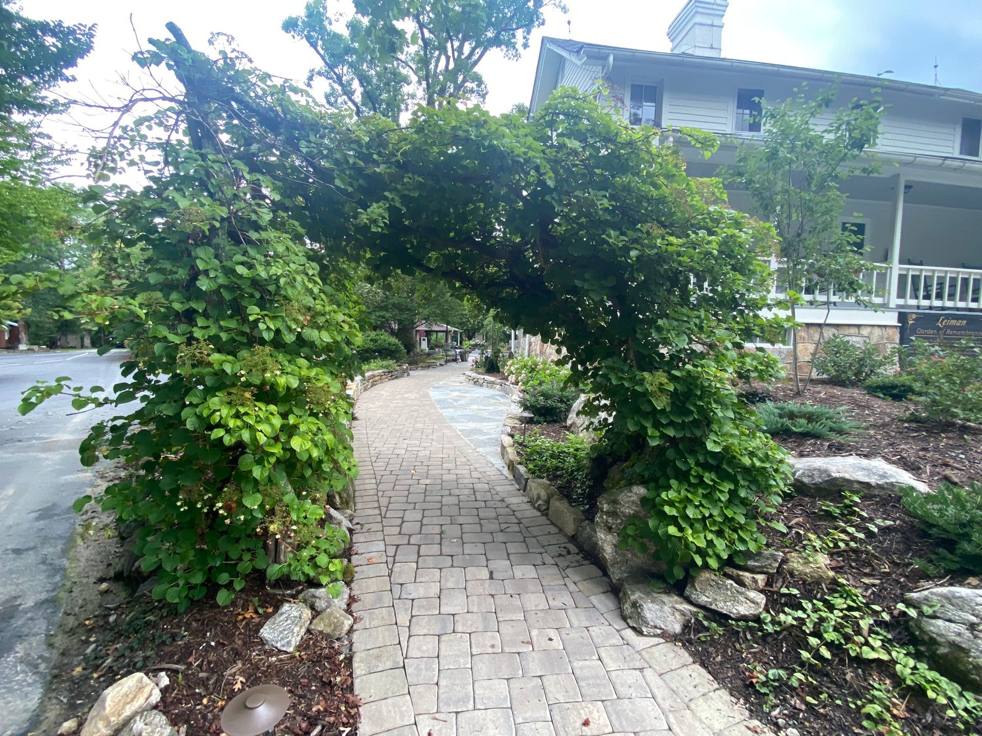 A brick walkway surrounded by trees and bushes in front of a house.