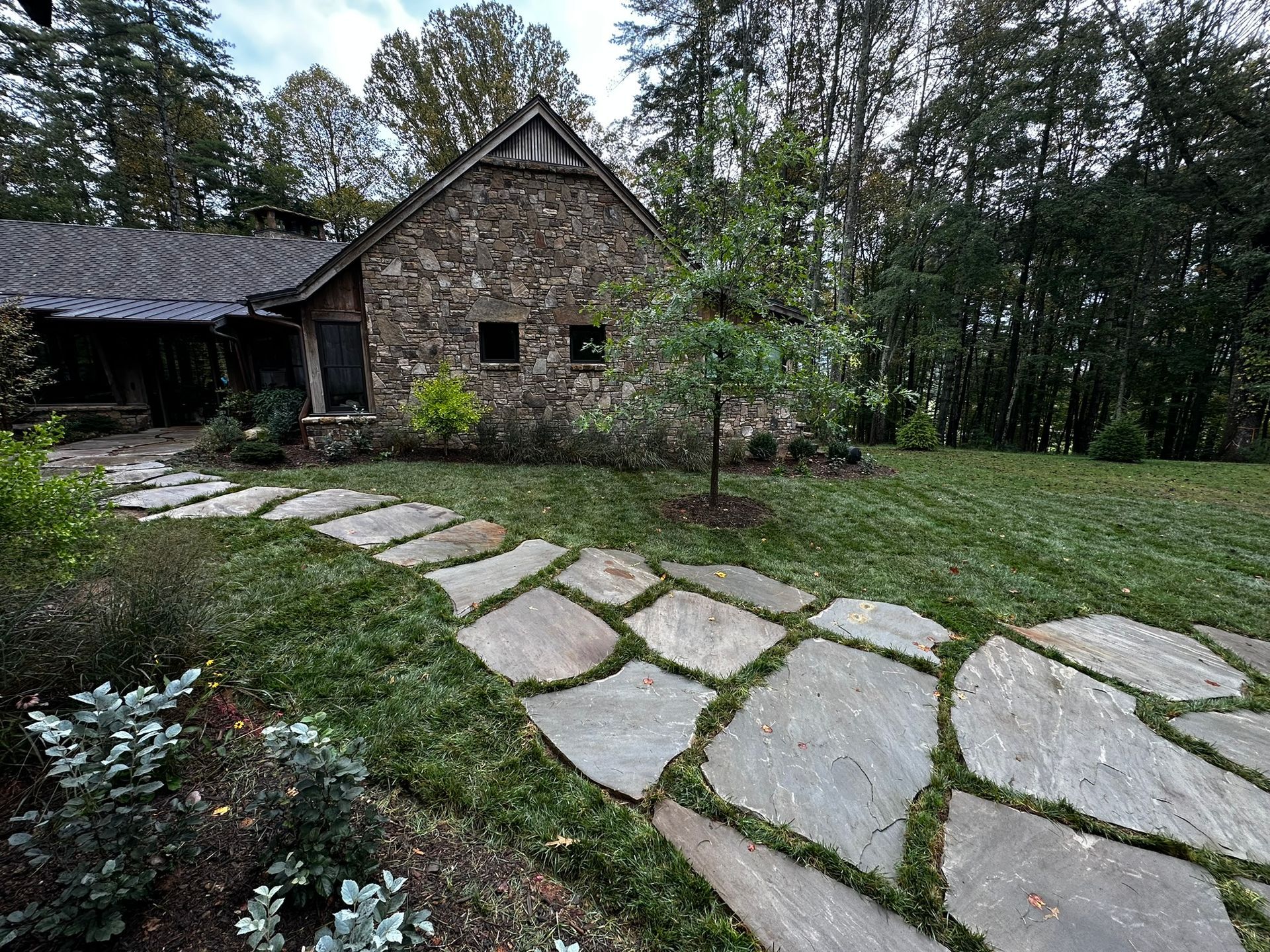 A stone walkway leading to a stone house in the woods.