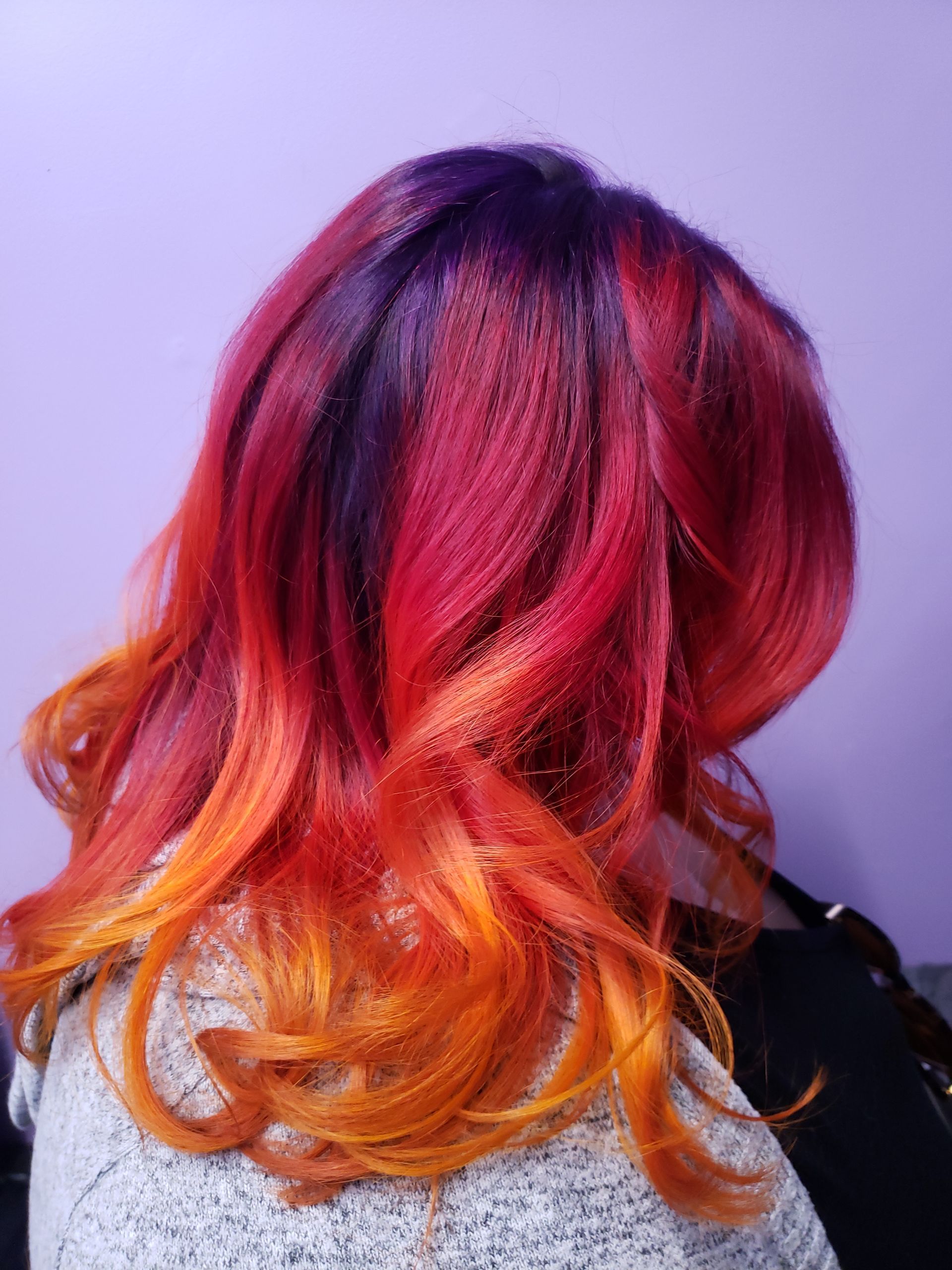 A woman with red and purple hair is wearing a grey sweater.