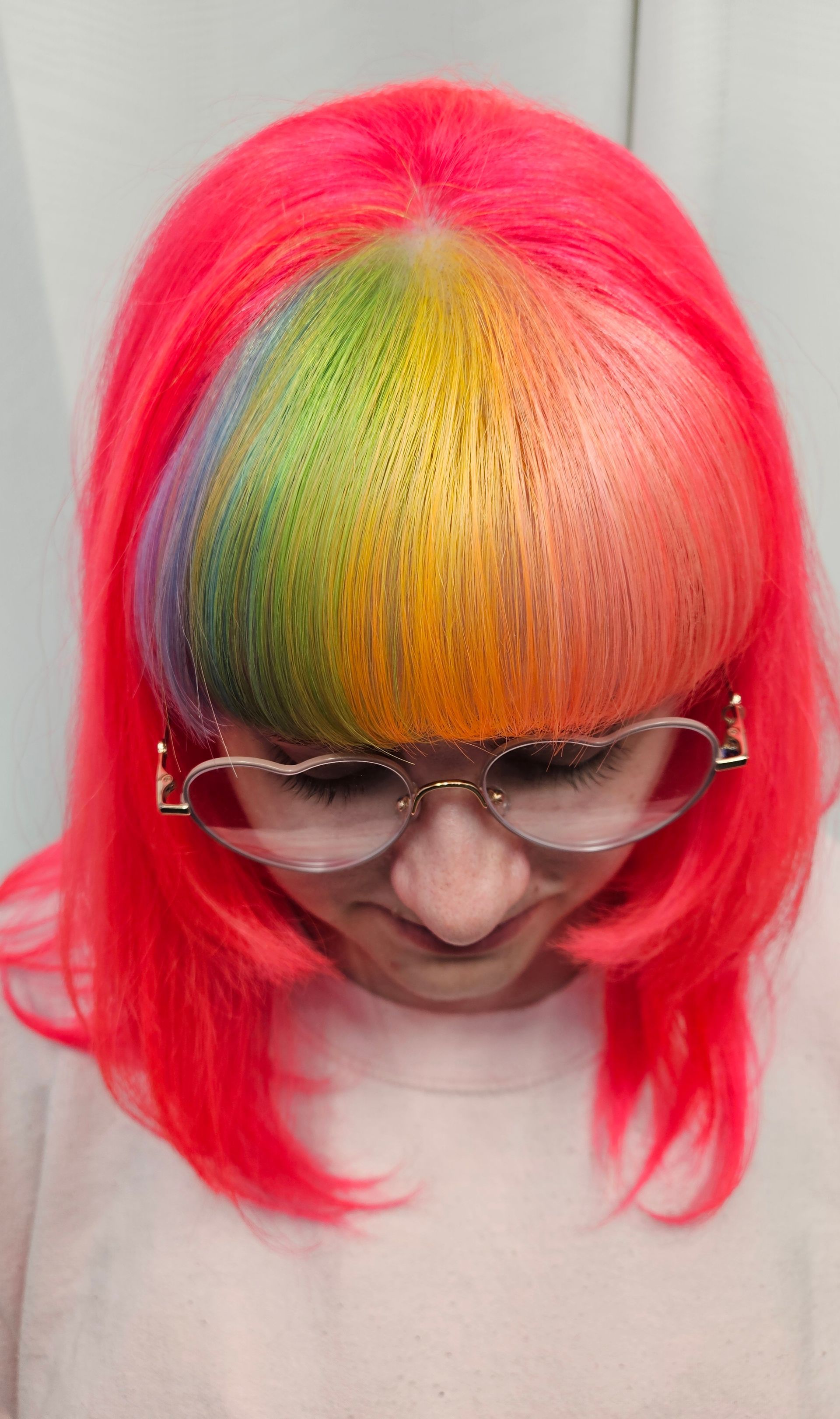 A woman with red hair and glasses has a rainbow in her hair.