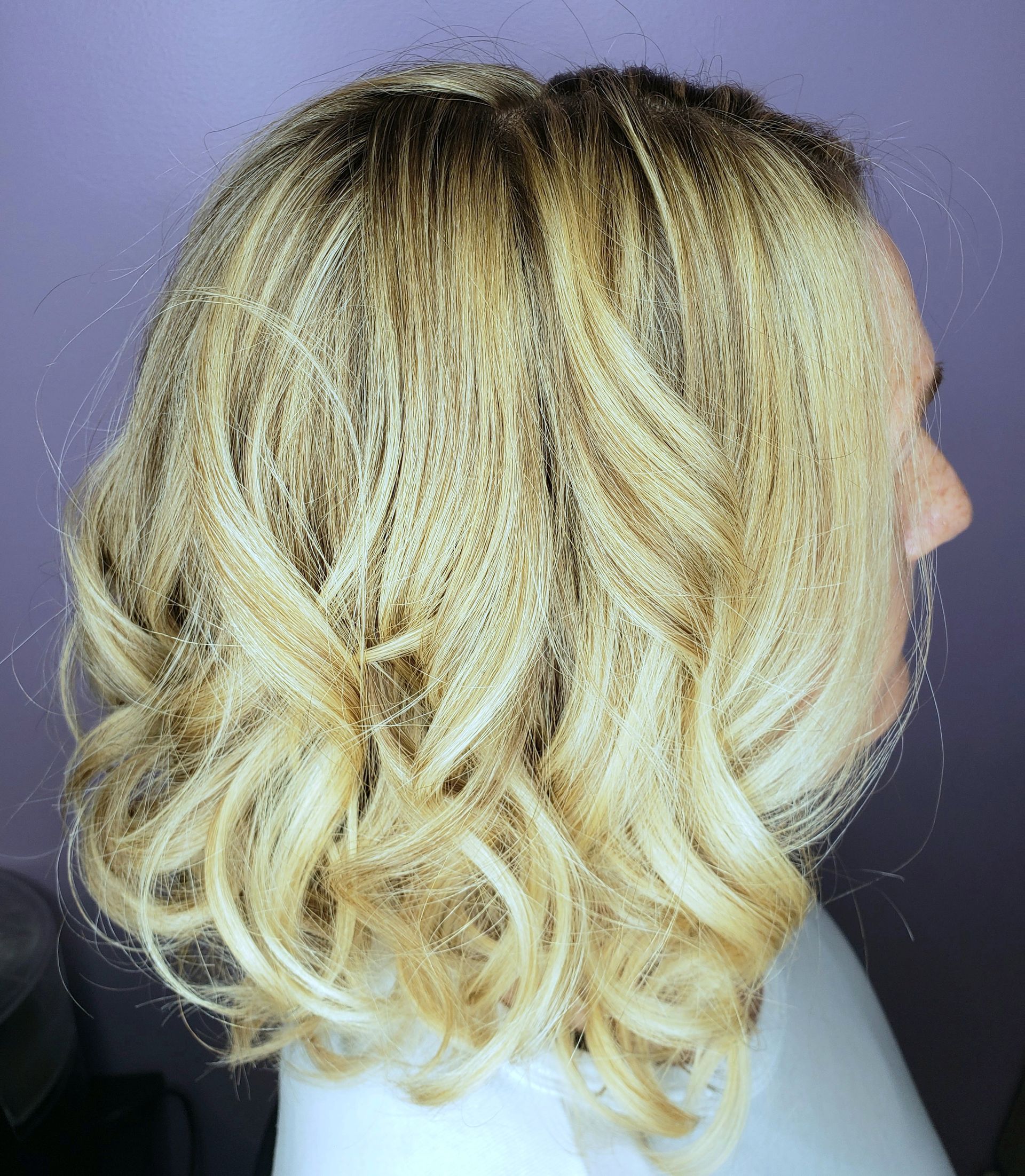 A woman with blonde curly hair is standing in front of a purple wall.