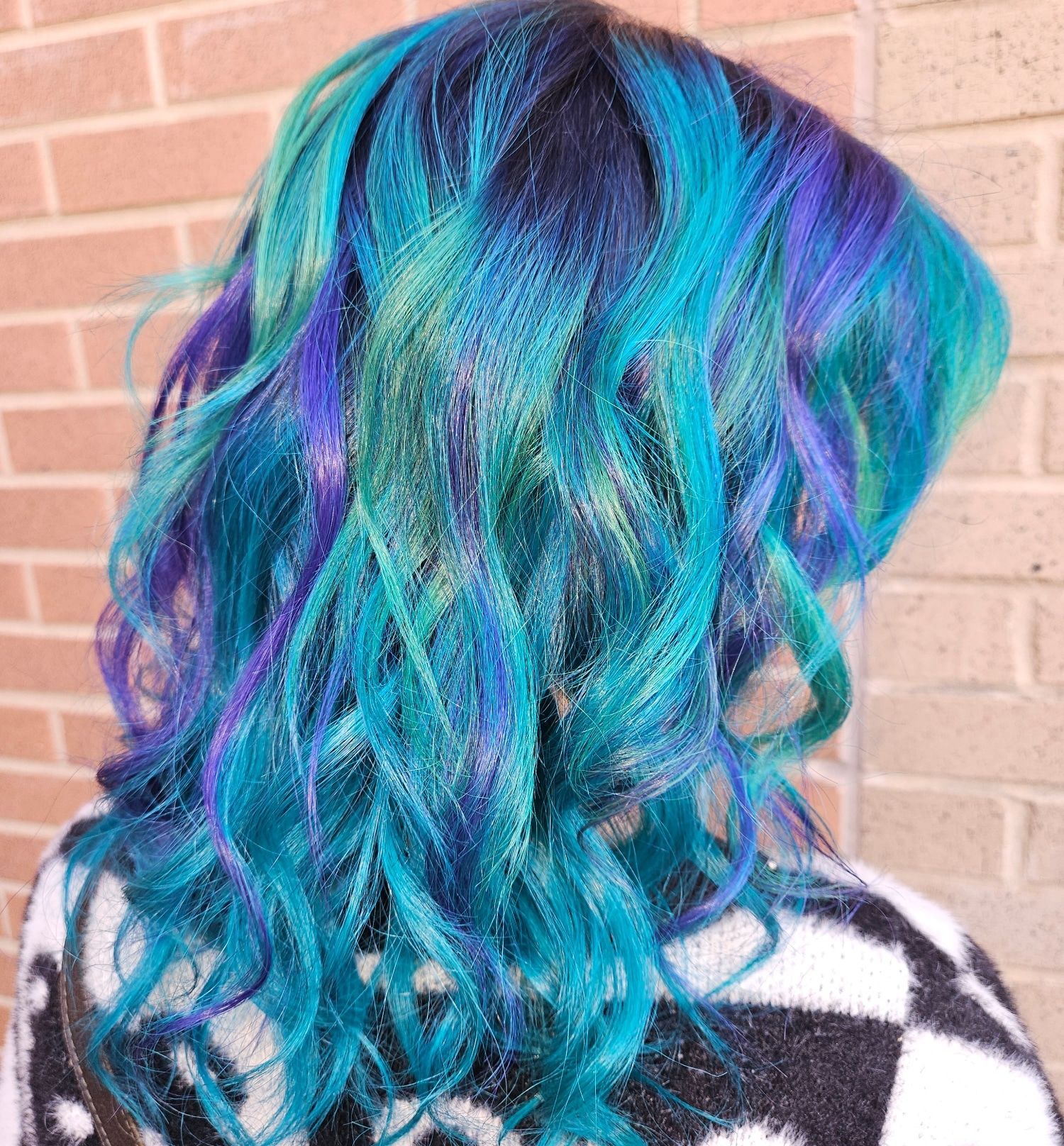 A woman with blue and purple hair is standing in front of a brick wall.
