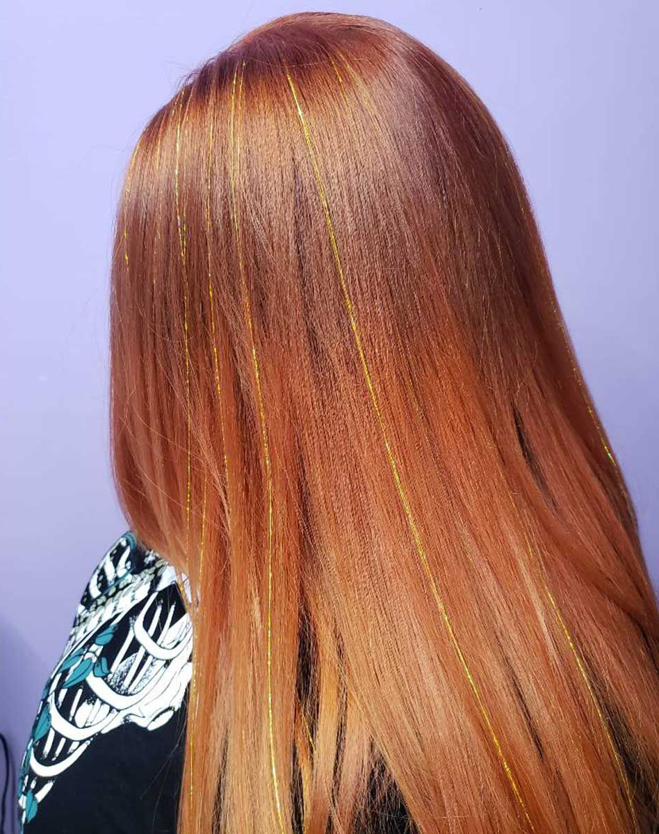 The back of a woman's head with long red hair and gold tinsel.