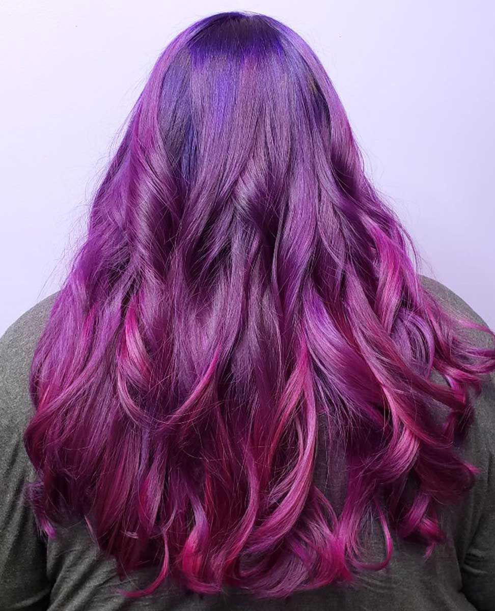 A woman with long purple hair is wearing a green shirt.