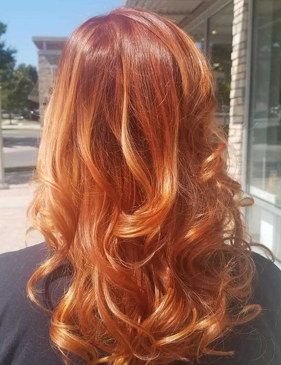 A woman with long copper hair color is standing in front of a building.
