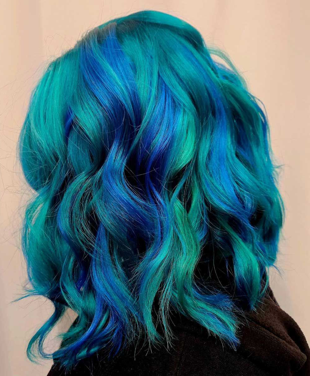 A woman with blue and green hair is wearing a black sweater.