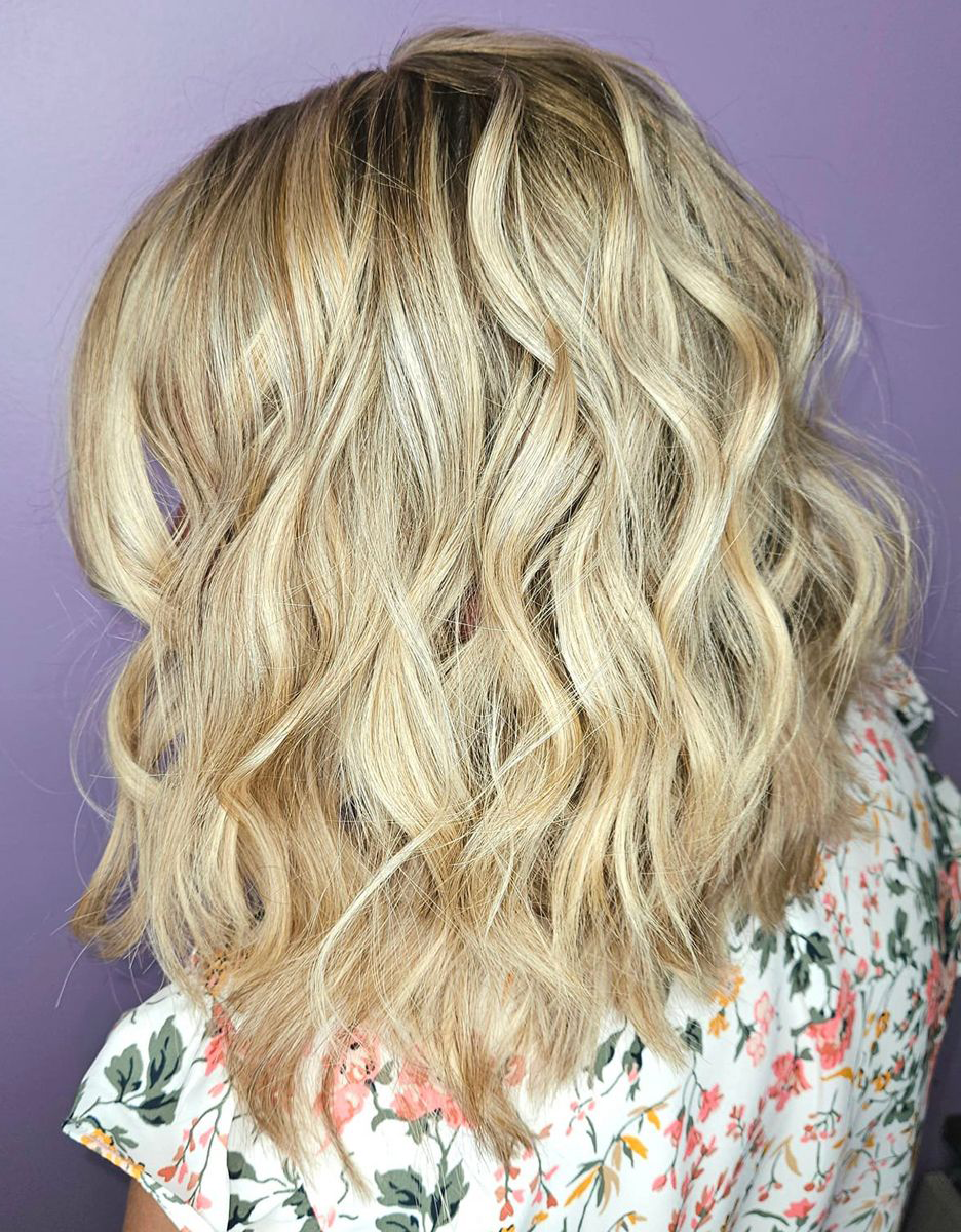A woman with blonde wavy hair is wearing a floral shirt.