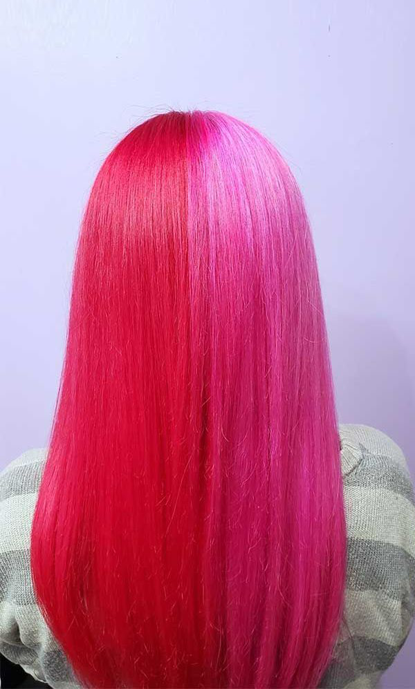 A woman with bright pink hair is sitting in front of a purple wall.