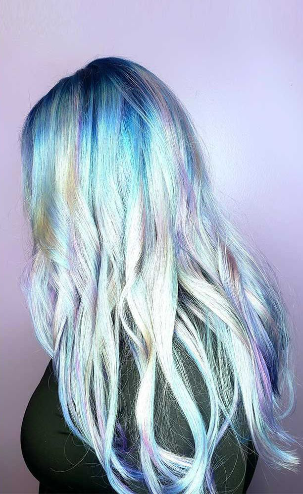 A woman with long blue and purple hair is standing in front of a purple wall.