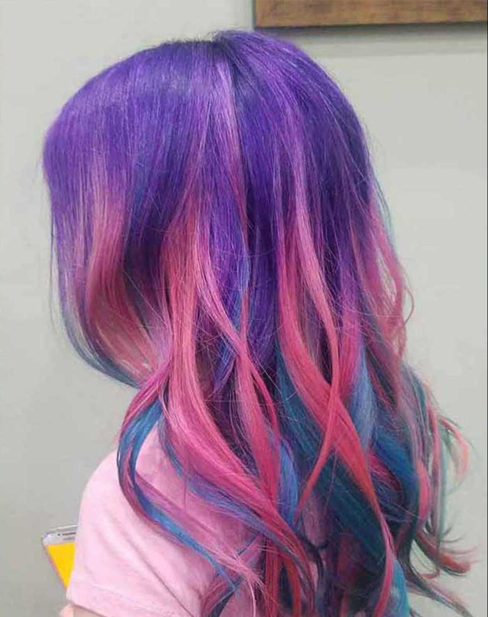 A woman with purple, pink, and blue hair is wearing a pink shirt.