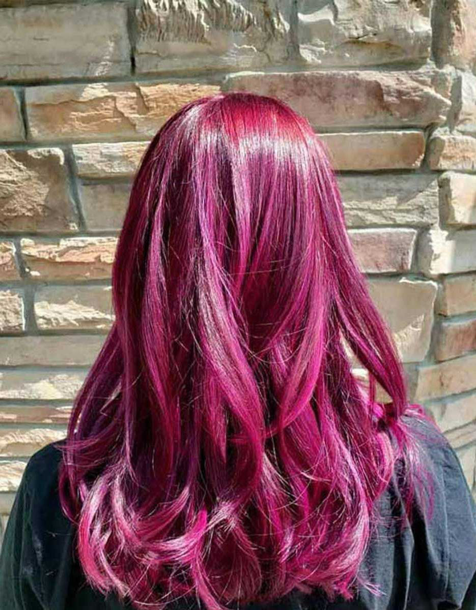 A woman with purple hair is standing in front of a brick wall.