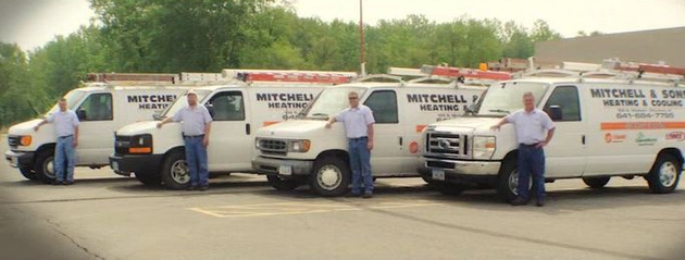 Four white Mitchell’s U.S. vans parked in a row with drivers standing beside them outdoors.