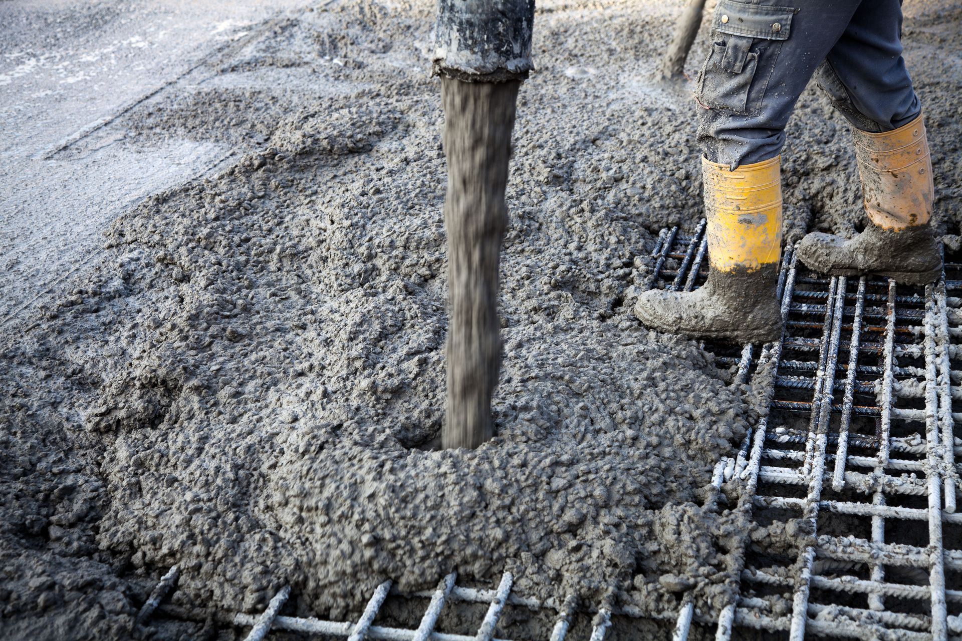 Concrete being poured over steel rebar, with a worker in yellow boots leveling it on a construction site.