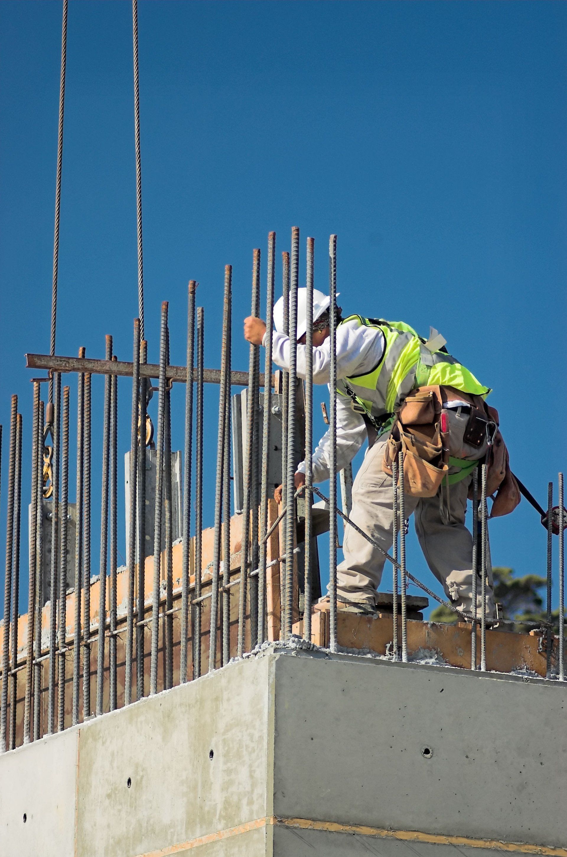 Construction workers on a concrete wall, tying rebar at a building site under a blue sky