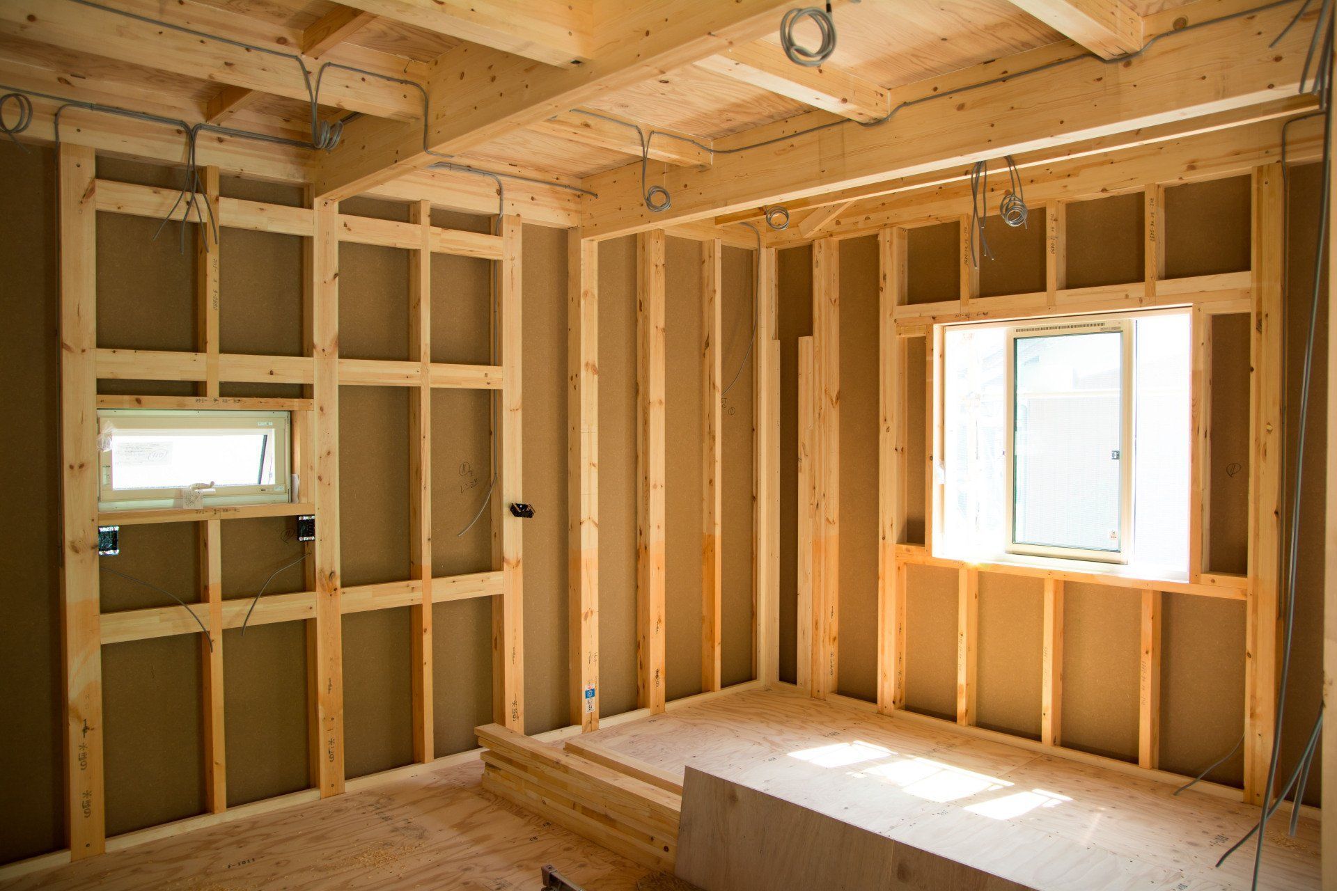 Unfinished room framed with exposed wood studs, two windows, and a simple bed frame or platform bed.