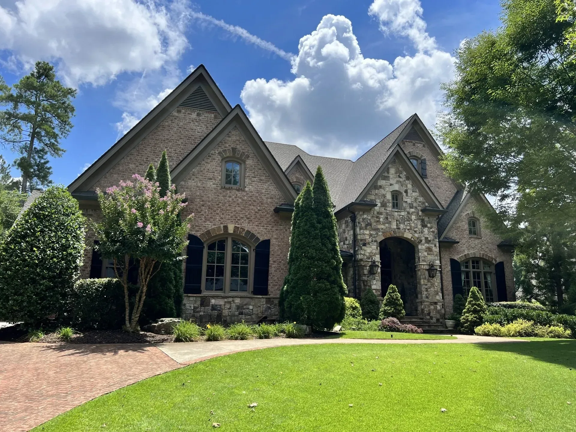 Brick and stone house with a green lawn and blue sky.