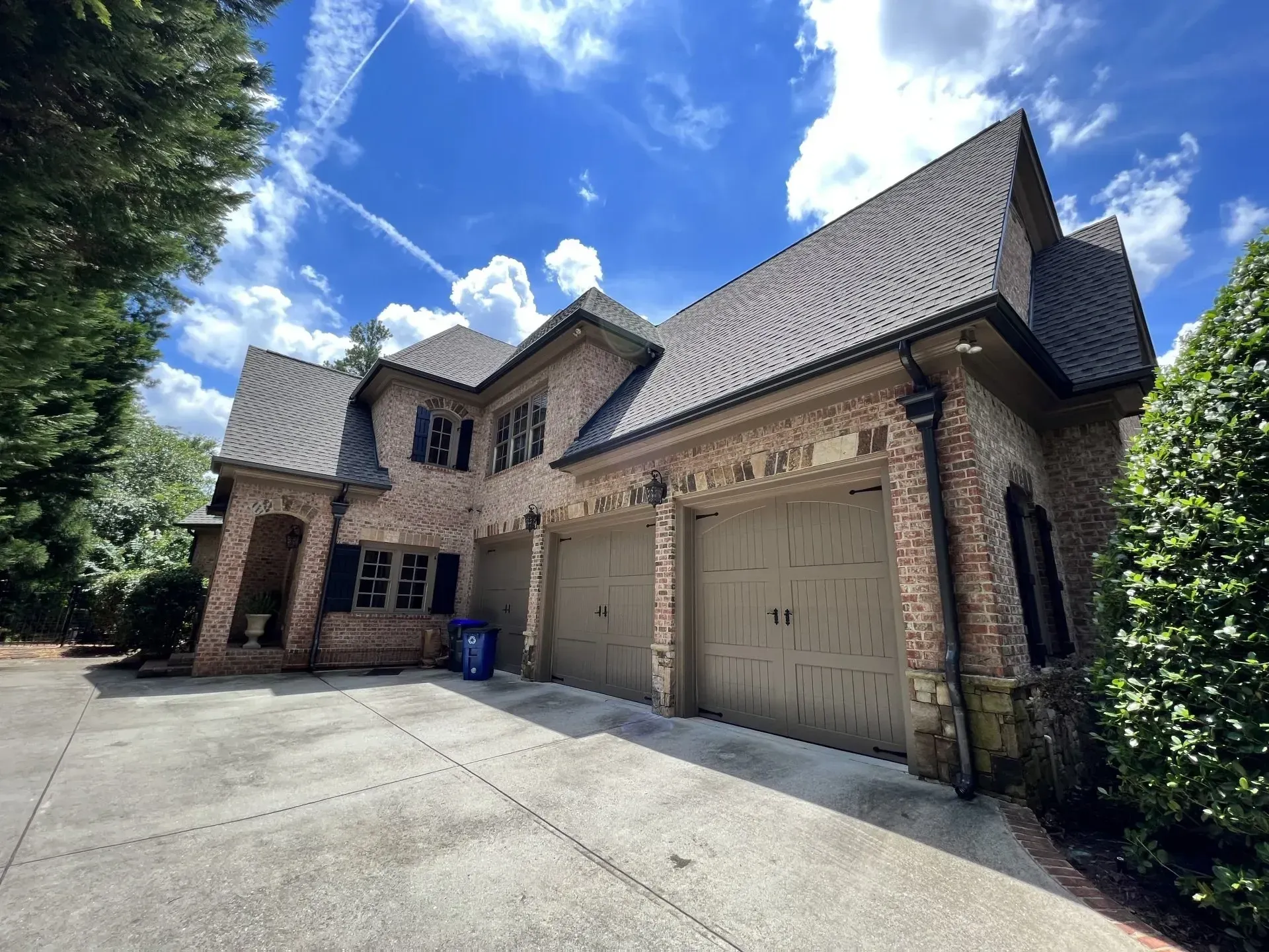 Brick home with brown roof, three-car garage, and blue sky.