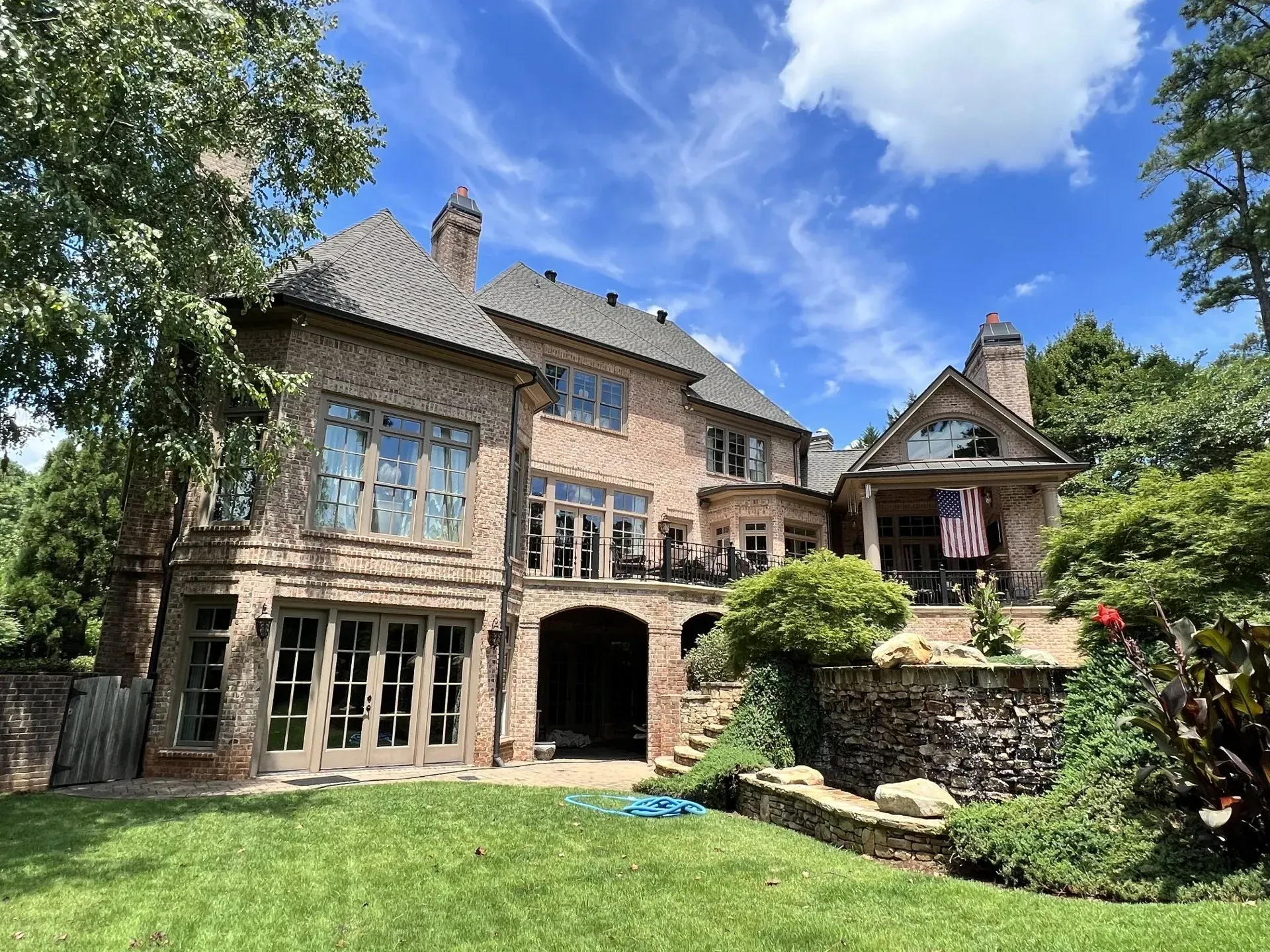Brick home with arched entryway and multiple windows, lush green lawn, sunny day.