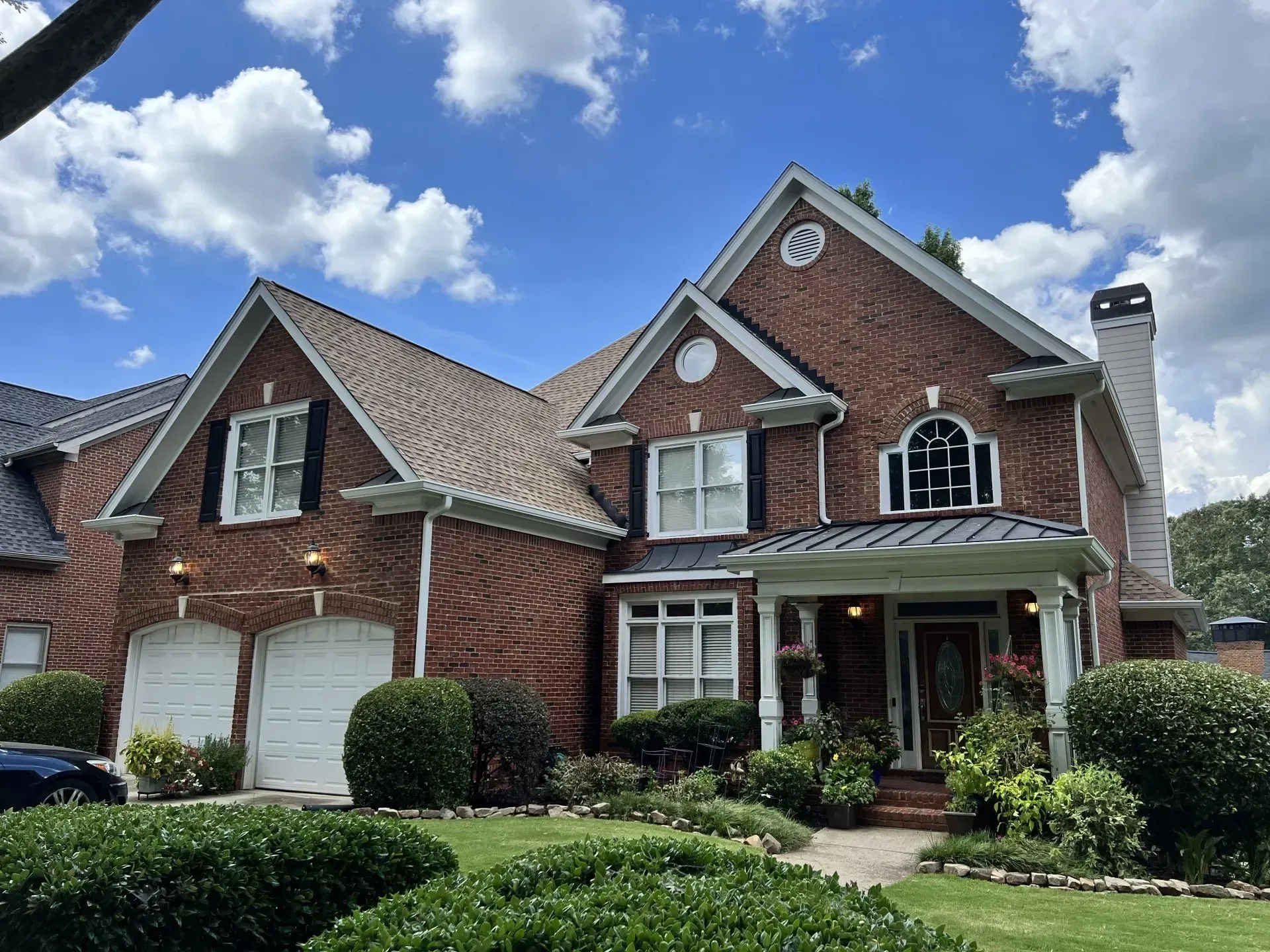 Brick house with multiple gables, white trim, and a covered front porch under a partly cloudy blue sky.