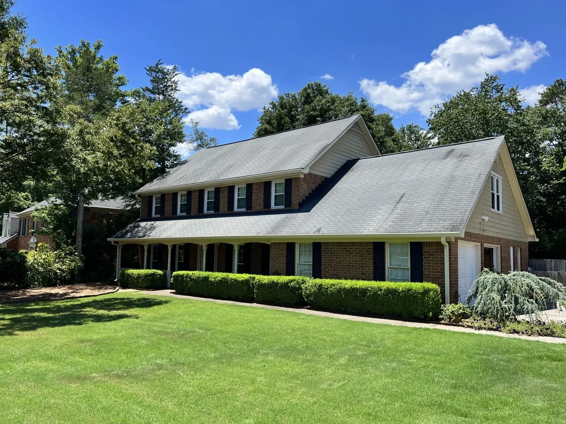 Two-story brick house with black shutters, green lawn, and blue sky.