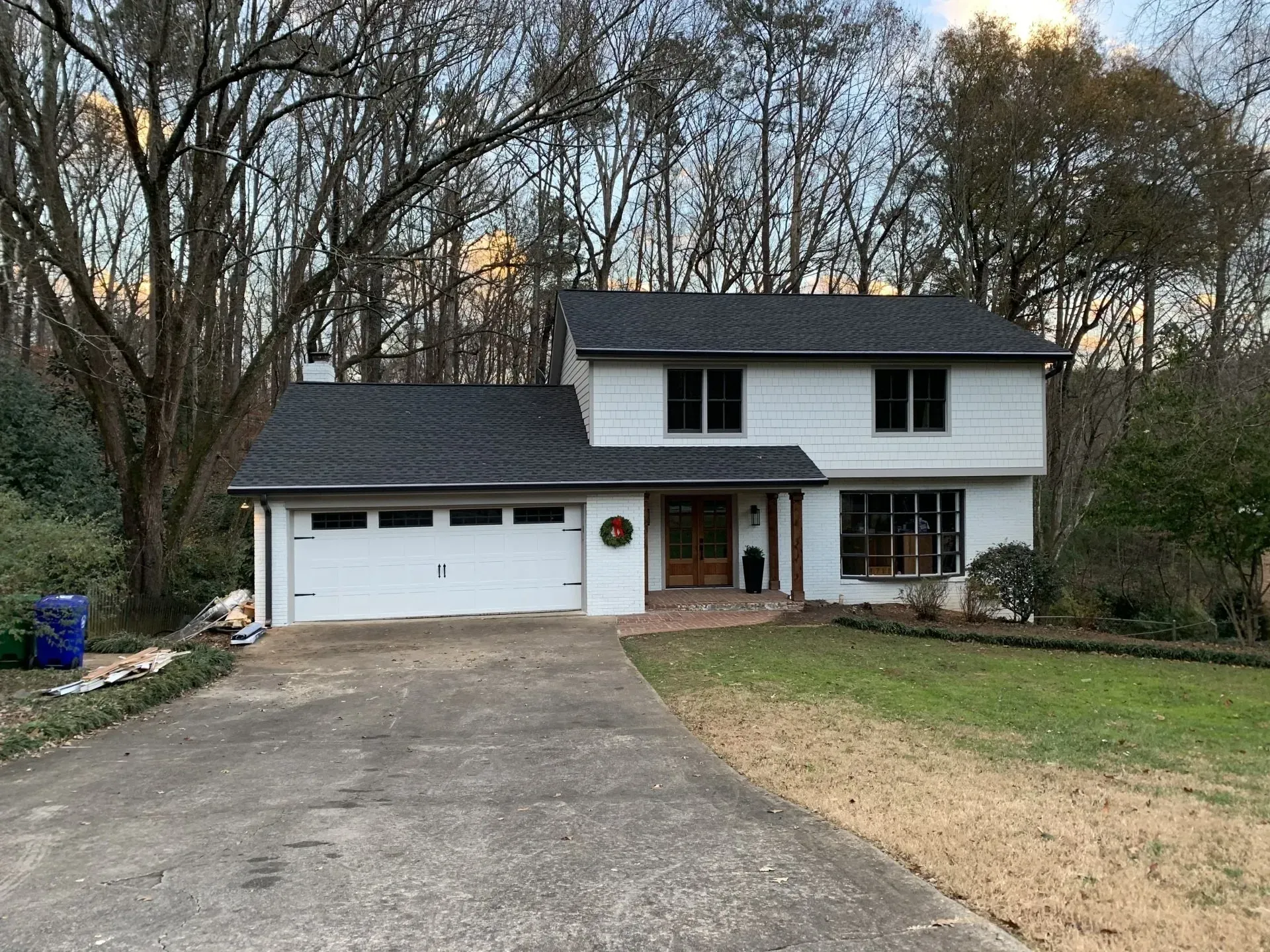 White house with a dark roof and a gray driveway. Green grass and trees surround it.