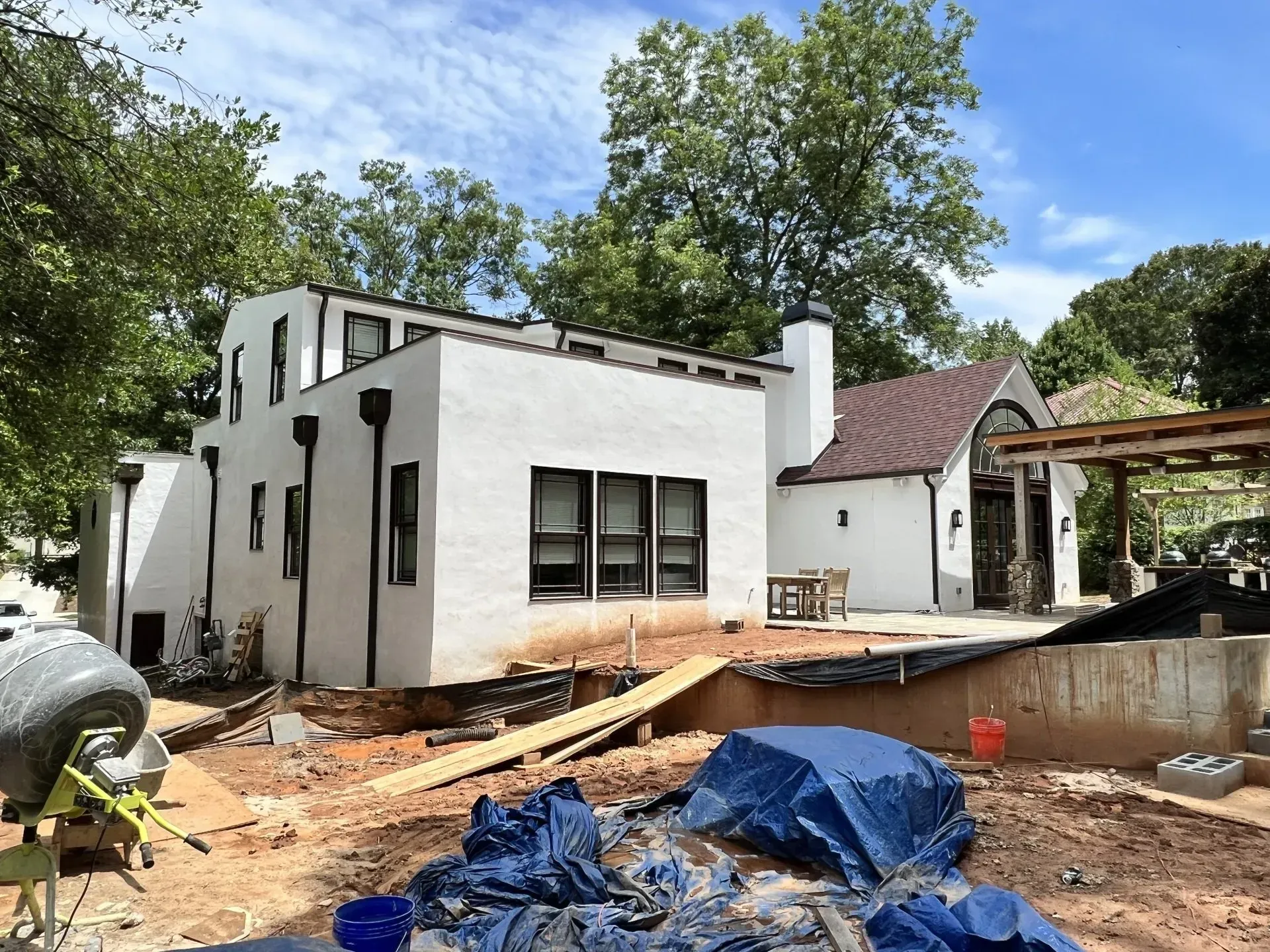 Construction site: white house with black trim, dirt ground, and blue tarp.